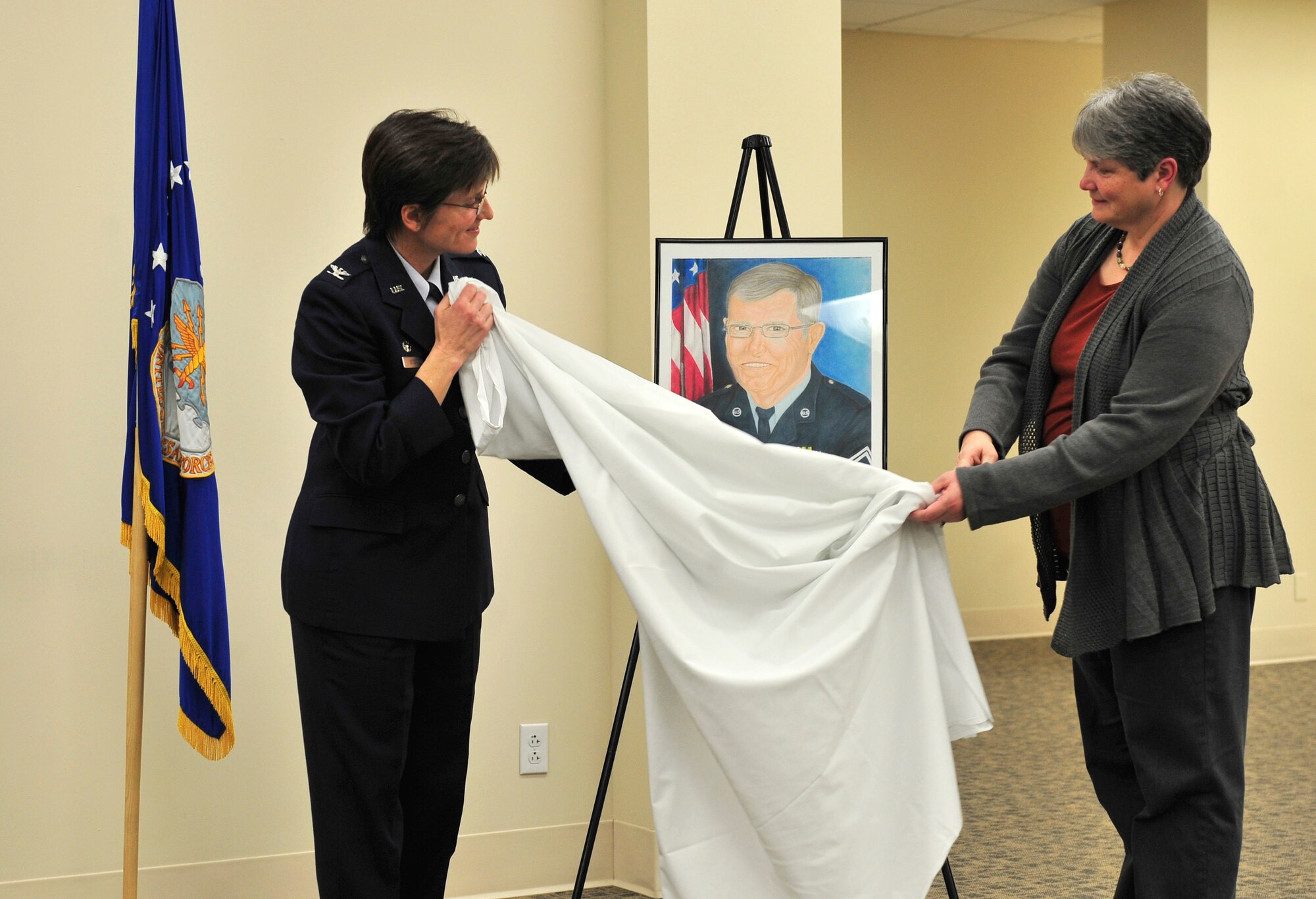 Col. Jill Sterling, 375th Medical Group commander and Gloria Lima unveil a painting of retired chief Rodney Deltgen during a hospital auditorium dedication ceremony Feb. 10. Lima is the daughter of Deltgen and the auditorium will be renamed after him. The painting is a gift to her from the 375 MDG. (U.S. Air Force photo/ Staff Sgt. Stephenie Wade)