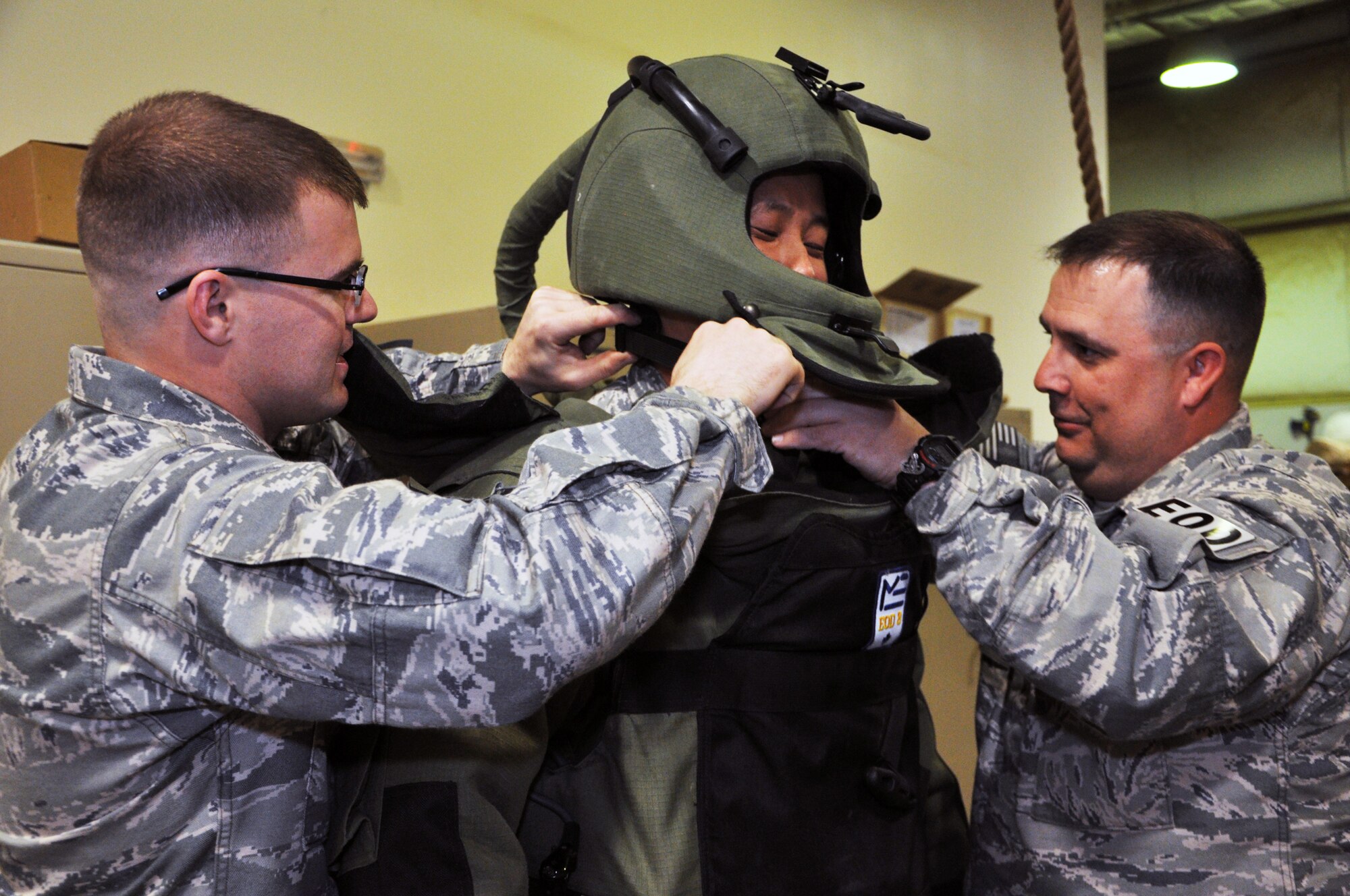 Staff Sgt. Ryan Johnson and Master Sgt. Jack Burleigh, 332nd Expeditionary Civil Engineer Squadron Explosive Ordnance Disposal members, help Maj. Young Han, 332nd Air Expeditionary Wing protocol chief, into the bomb suit during an EOD tour Feb. 17, 2012 at an undisclosed location in Southwest Asia. The bomb suit weighs about 70 pounds and protects from blast overpressure, fragmentation, heat and flames. Han is deployed from Hill Air Force Base, Utah, and is a native of Cincinnati. Johnson is deployed from Misawa Air Base, Japan. Burleigh is deployed from Nellis Air Force Base, Nev. (U.S. Air Force photo by Senior Airman Melanie Holochwost/Released)
