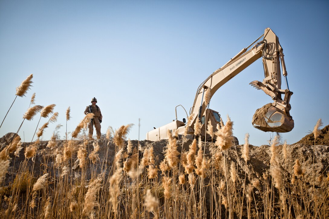 Lance Cpl. Timothy Haerr, a combat engineer with Bridge Platoon, Alpha Company, 9th Engineer Support Battalion and a native of Chicago, provides security as an excavator removes dirt to prepare an area for the construction of a bridge near Combat Outpost Rankel in the district of Garmsir, Helmand province, Jan. 29. The Marines of Bridge Platoon endured a 5-day convoy in order to replace a temporary bridge with a more permanent structure that would increase mobility for Marines operating in the area.