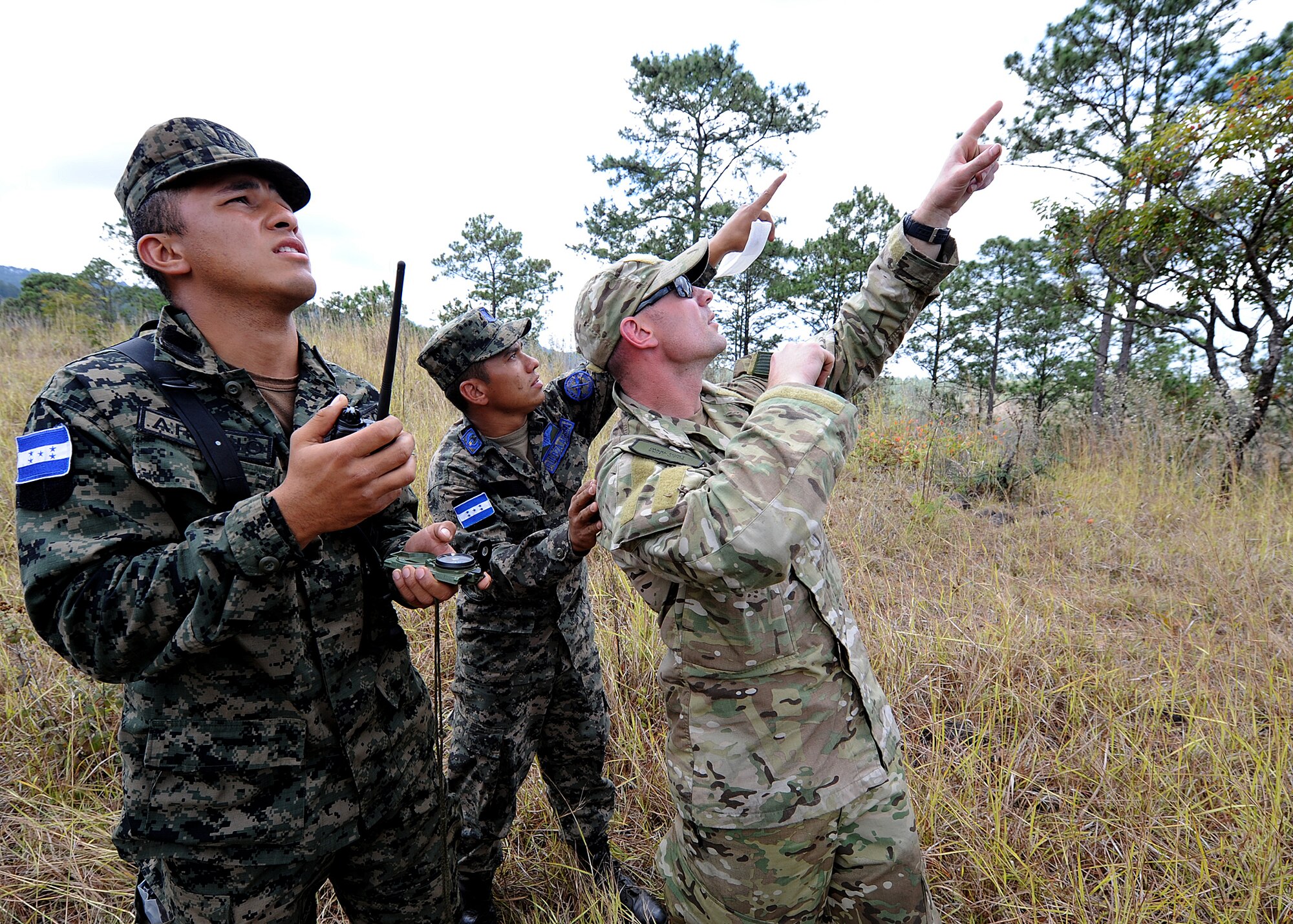 A Honduran Air Force air crew member and Staff Sgt. Daniel Foret, 571st Mobility Support Advisory Squadron Survival, Evasion, Resistance and Escape specialist air advisor, locate a passing aircraft as a soldier from the Honduran army's unit TESON communicates their position to the pilot during the vectoring application of the aircrew survival seminar at Tamara, Honduras, Feb. 15.  (U.S. Air Force photo by Tech. Sgt. Lesley Waters)