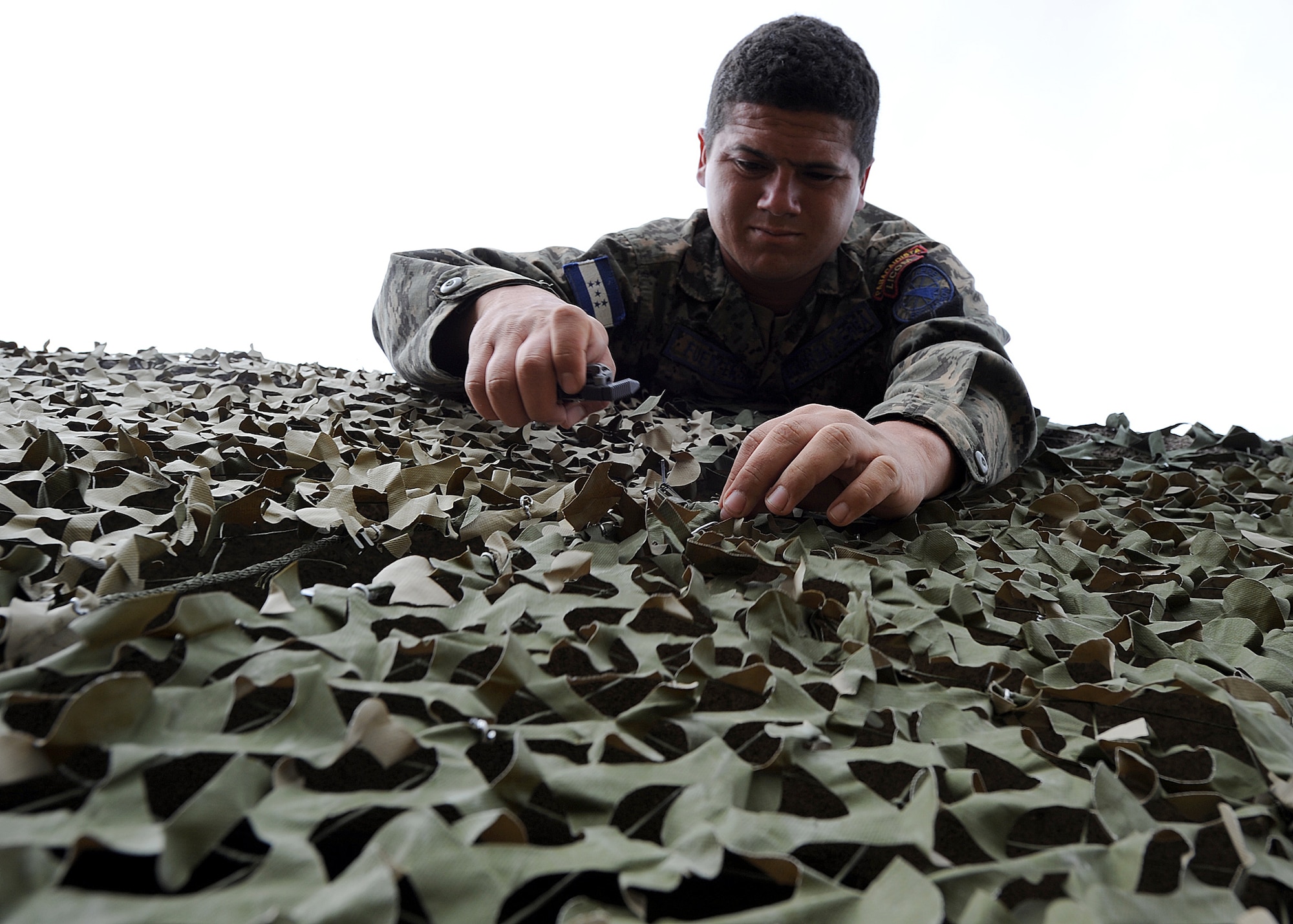 Staff Sgt. Miguel Fuentes, Honduran Air Force security forces member, secures two camouflage nets together as part of the tactical communication portion of the air base defense seminar Feb. 8, during the Air Mobility Command Building Partner Capacity mission in Tegucigalpa, Honduras.  (U.S. Air Force photo by Tech. Sgt. Lesley Waters)