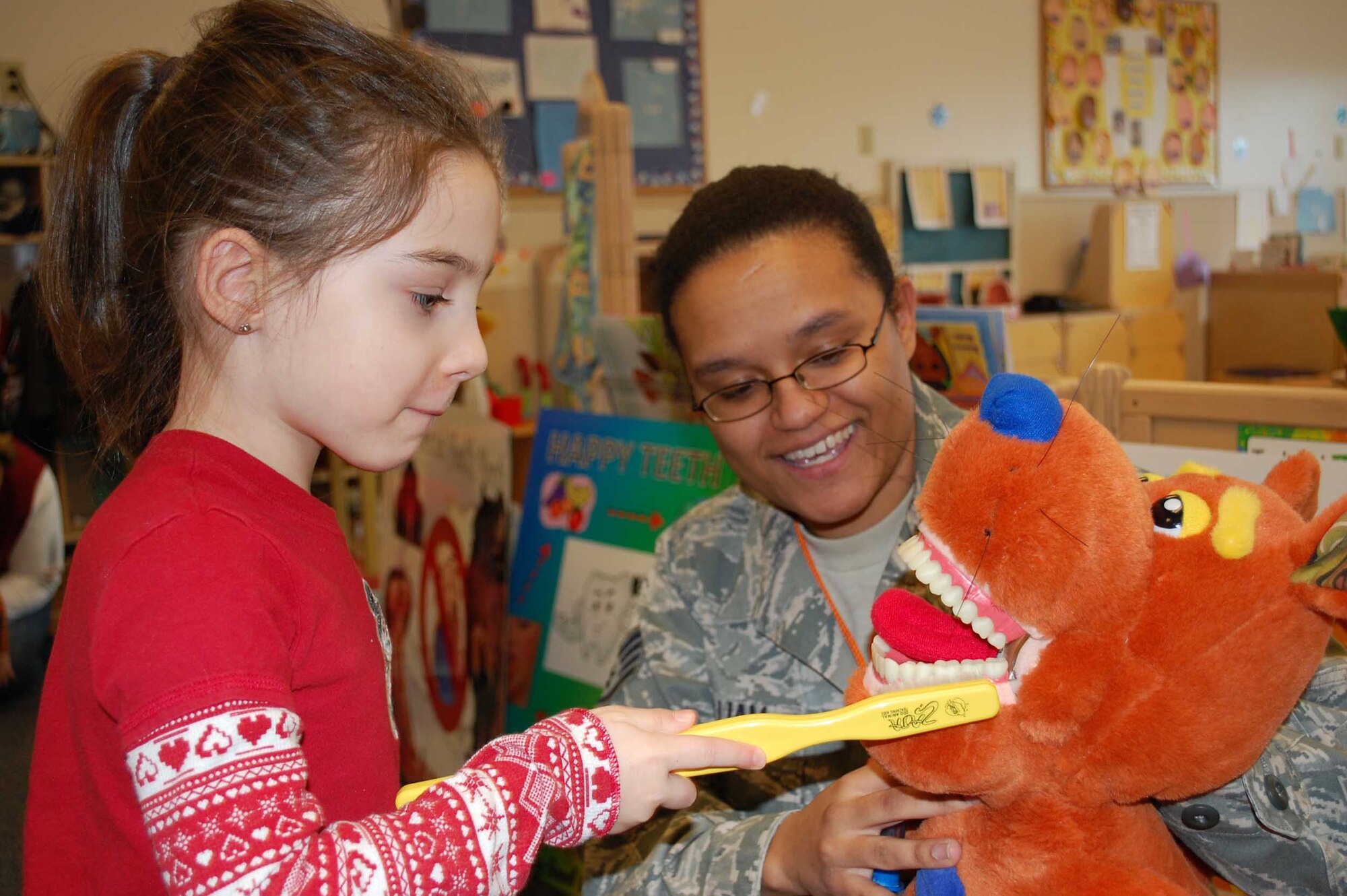 After listening to the staff from the Dental Clinic explain important information about dental health, Emily Nissen, 4, demonstrates how to brush teeth with the help of Pulliam. (U.S. Air Force photo/Senior Airman Reggie Manning)