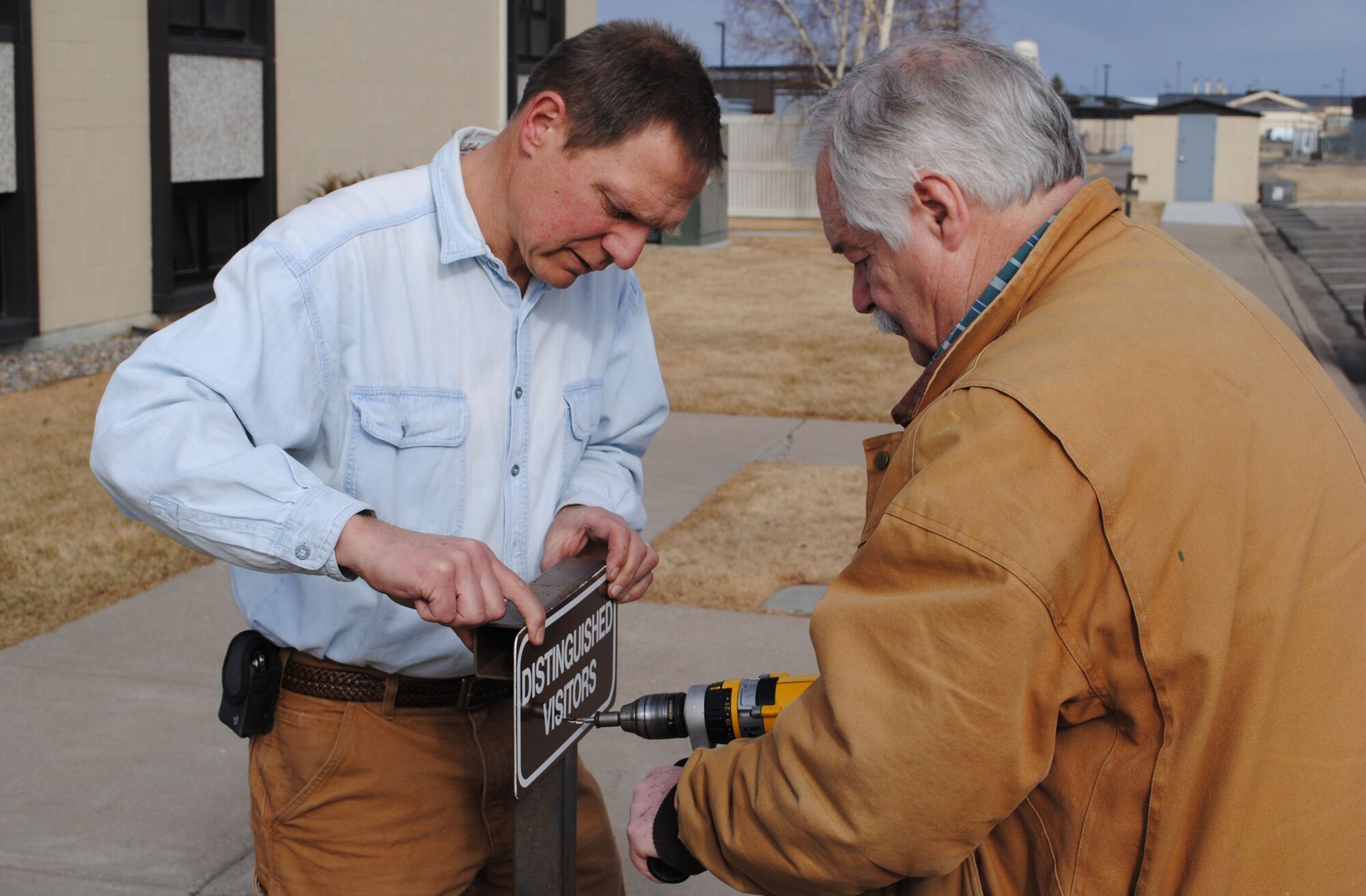 Dave Chandler, 341st Civil Engineer Squadron sign shop member, holds a distinguished visit sign in place as Cliff Holmes, 341st CES sign shop member, attaches it. Chandler and Holmes created the sign in a matter of minutes. (U.S. Air Force photo/Airman 1st Class Cortney Paxton)