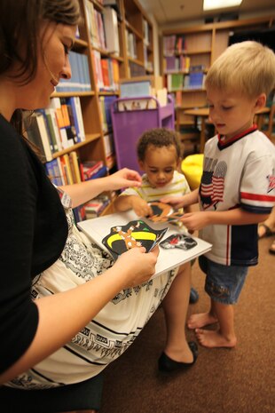 Lori Bradford, a librarian aid at the station library, holds a illustration board to follow along with a nursery rhyme as Dariuse Forrester, 19 months and Wyatt Plumley, 4, interact with the characters of the rhyme during the bi-monthly preschool storytime session, Aug. 11.
