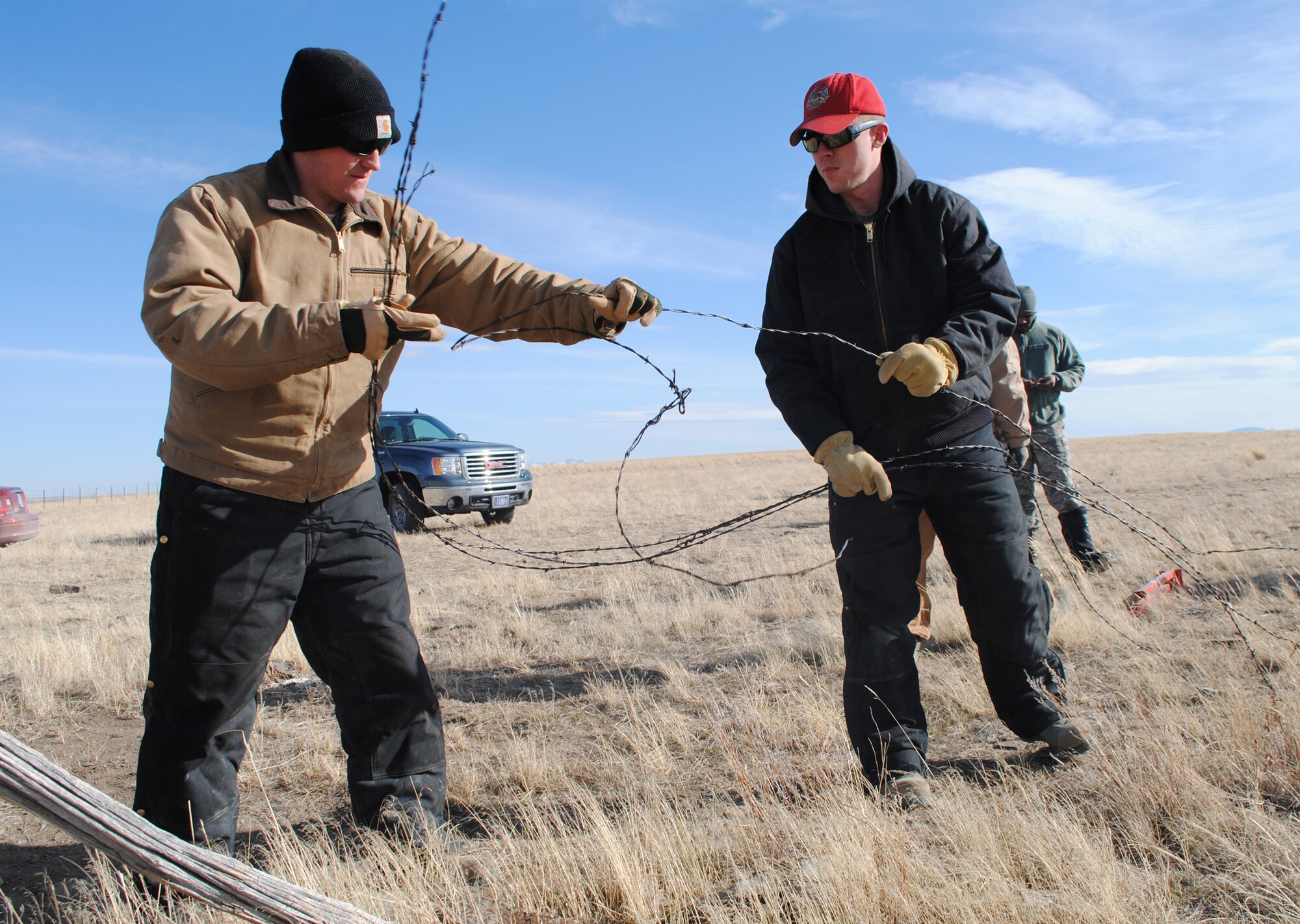 Senior Airmen Joseph Bennett, left, and Adam Dunkerton, both 819th RED HORSE Squadron pavement and equipment apprentices, begin rolling up old barbed-wire fencing. Both are a part of an ongoing, five-mile fencing project at the First Peoples Buffalo Jump State Park near Ulm. (U.S. Air Force photo/Airman 1st Class Katrina Heikkinen)