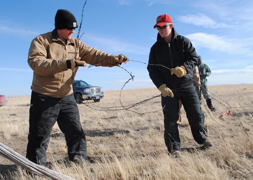 Senior Airmen Joseph Bennett, left, and Adam Dunkerton, both 819th RED HORSE Squadron pavement and equipment apprentices, begin rolling up old barbed-wire fencing. Both are a part of an ongoing, five-mile fencing project at the First Peoples Buffalo Jump State Park near Ulm. (U.S. Air Force photo/Airman 1st Class Katrina Heikkinen)