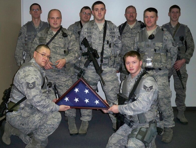 Members of the 213th Space Warning Squadron hold the new American flag that was sent to Annette Cook, a childhood friend of Alaska Air National Guard Tech. Sgt. Ricky Ramos, to replace the flag damaged in an explosion that destroyed Cook’s Butler County, Kan., home. Pictured back row, left to right: Staff Sgt. Joseph Brokus, Staff Sgt. William Stead, Tech. Sgt. Christoph Albritton and Staff Sgt. Benjamin Drake. Middle row, left to right: Staff Sgt. Matthew Powell, Staff Sgt. Thomas Elliott and Staff Sgt. Robert Ives. Front row, left to right: Tech. Sgt. Ricky Ramos and Senior Airman Justin Smith. The team volunteered their time, money and effort to replace the military decorum that Cook lost in the explosion. (U.S. Air Force photo)