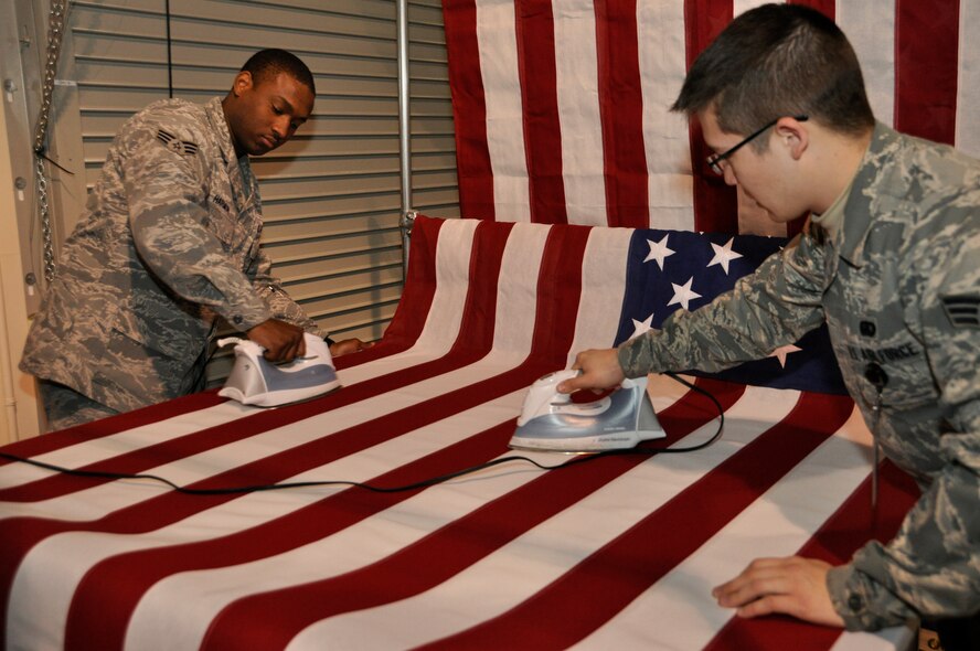 Senior Airman Darron Harmon, 512th Memorial Affairs Squadron, and Senior Airman Matthew Siegele, 627th Force Support Squadron, iron a U.S. Flag Feb. 13, 2012, at the Charles C. Carson Center for Mortuary Affairs, Dover Air Force Base, Del. Harmon and Siegele are deployed here in support of the mortuary mission. They work in the departures section where fallen heroes are placed in a casket chosen by their family. A flag is then draped over the casket before the fallen begin the journey home to their final resting place. (U.S. Air Force photo/Christin Michaud)