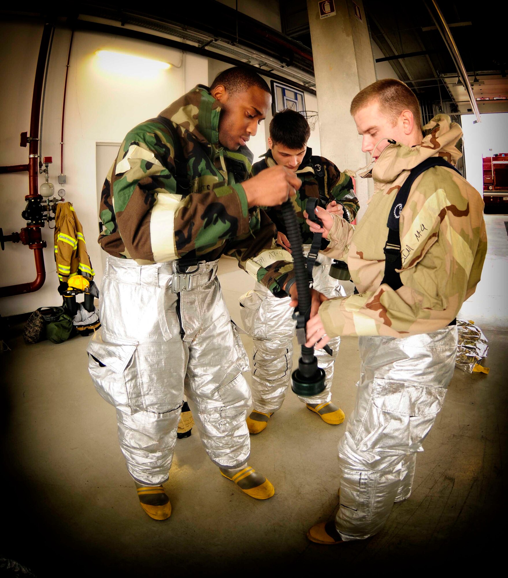 (From Left) Staff. Sgt Derek White,31st Civil Engineer Squadron firefighter,shows Airmen 1st Class Ronald Brown and Benjaming Reed 31st CES firefighters,how to adjust their straps for a breathing hose connection Feb.23 at Aviano Air Base, Italy. The firefighters don their mission oriented protective posture gear to conduct a training scenario in preparation for the upcoming Operation Readiness Exercise.  (U.S. Air Force photo/Airman 1st Class Briana Jones)