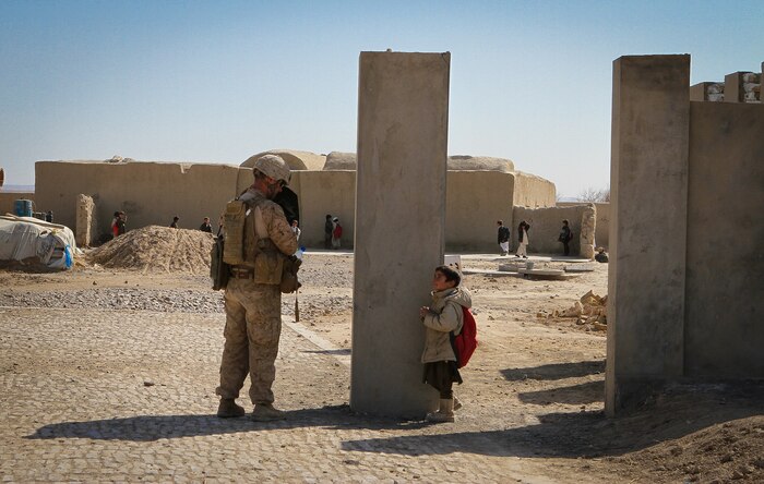 A young student standing outside the grade school here greets Cpl. Joshua Brooks, a Marine serving with Team 3, Civil Affairs Detachment 11-2, as Brooks patrols into the school grounds Feb. 25, 2012. The Marines of Team 3 provided guidance to the local government here to help them construct a new school. The current school is made of mud and mortar, is overcrowded and only has enough capacity to hold up to sixth grade. The new school will have up to eighth grade and have more than enough room for students and teachers. Brooks is from Celeste, Texas, and is serving under Regimental Combat Team 5 and alongside 1st Light Armored Reconnaissance Battalion in Helmand province.