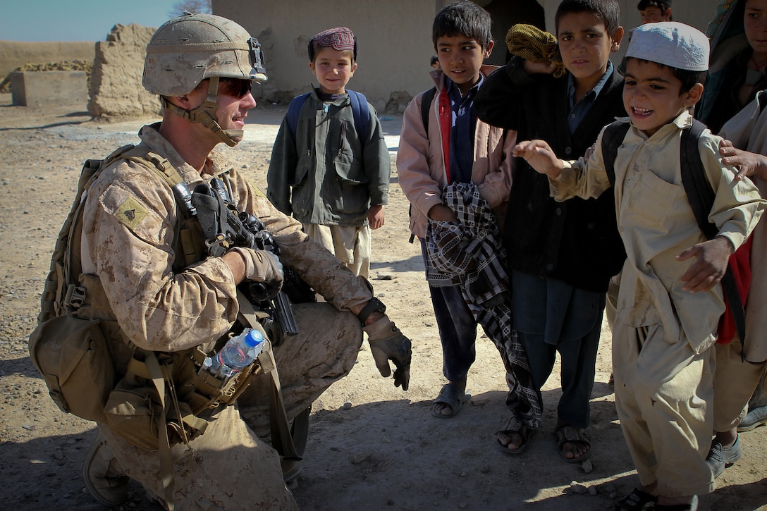 Corporal Joshua Brooks, a Marine serving with Team 3, Civil Affairs Detachment 11-2, greets students as they arrive for school here Feb. 25, 2012. The Marines of Team 3 provided guidance to the local government here to help them construct a new school. Brooks said visiting the school is the highlight of his deployment. The current school is made of mud and mortar, is overcrowded and only has enough capacity to hold up to sixth grade. The new school will have up to eighth grade and have more than enough room for students and teachers. Brooks is from Celeste, Texas, and is serving under Regimental Combat Team 5 and alongside 1st Light Armored Reconnaissance Battalion in Helmand province.