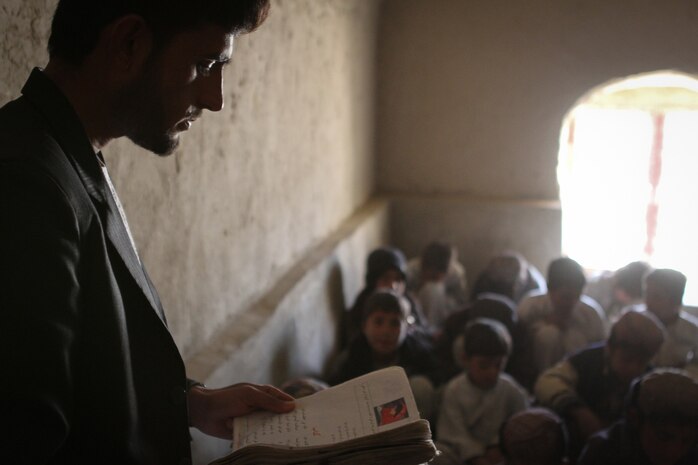 The head teacher at the school here follows along as his student recites a poem for the class Feb. 25, 2012. Marines serving with Team 3, Civil Affairs Detachment 11-2, are providing guidance to the local government here to help them construct a new school. The current school is made of mud and mortar, has no electricity or running water, is overcrowded and only has enough capacity to hold up to sixth grade. The new school will have up to eighth grade and have more than enough room for students and teachers.