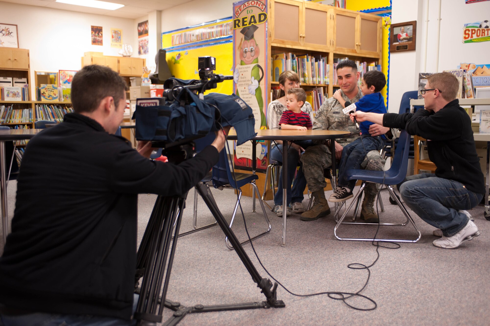 Zack Nugent (left), and Darren Leeds, from KEVN Black Hills Fox, conduct an interview with Staff Sgt. George Munoz, 28th Munitions Squadron weapon systems craftsman, and his family at the Robbinsdale Elementary School library in Rapid City, S.D., Feb. 17, 2012. KEVN covered Munoz’s surprise return home. (U.S. Air Force photo by Airman 1st Class Zachary Hada/Released)