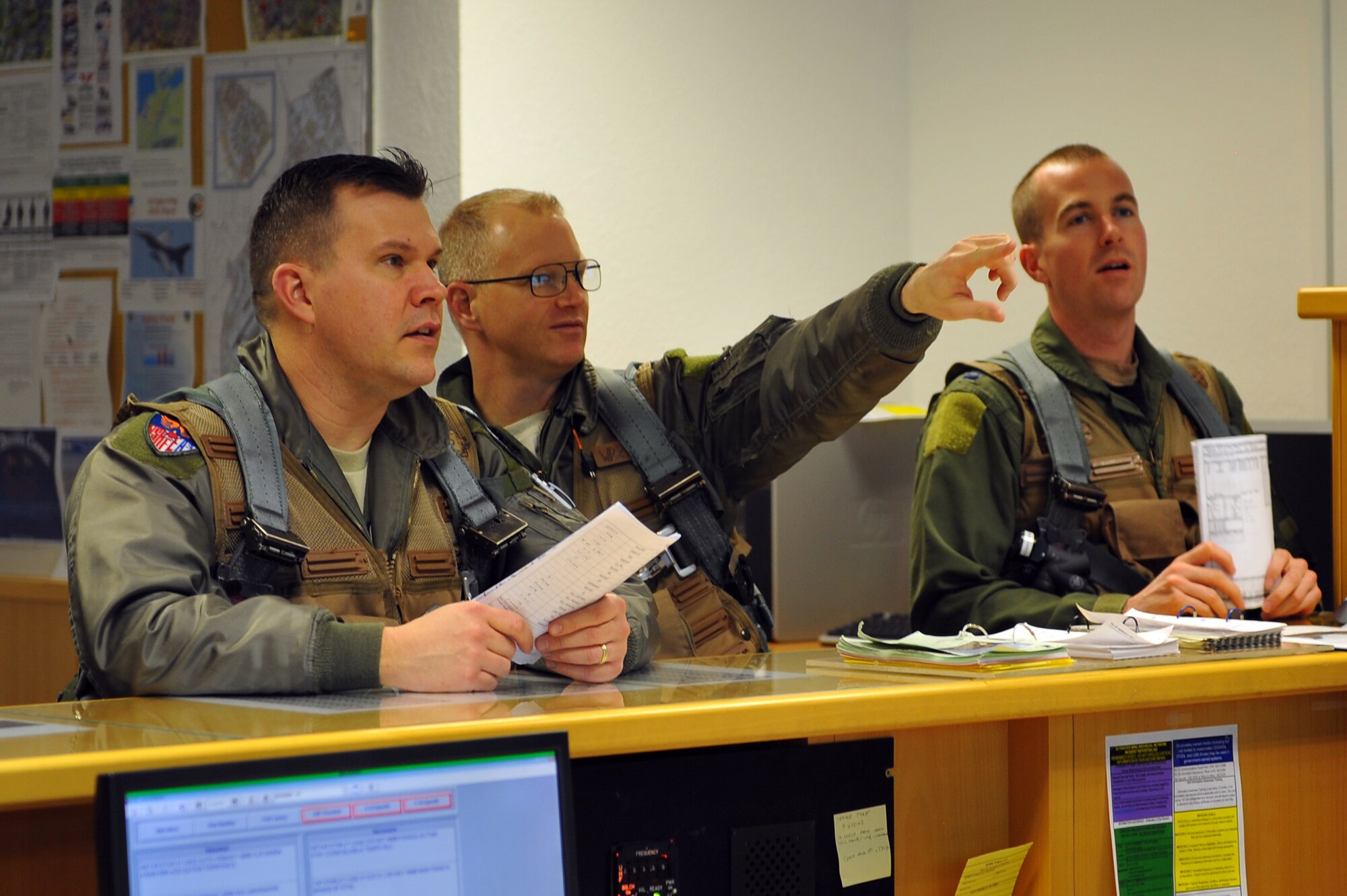 SPANGDAHLEM AIR BASE, Germany – Lt. Col. Robert Petty, left, U.S. Air Forces in Europe Standards and Evaluations Branch chief, Col. Chris Weggeman, center, 52nd Fighter Wing commander, and Capt. Mark Hickie, right, 52nd FW executive officer, read flight information and take notes before a briefing inside Bldg. 108 here Feb. 21. Twelve Airmen work at the squadron’s operations desk and are responsible for coordinating with base operations, weather operations and aircraft maintenance to ensure flight operations run smoothly. The operations desk is also responsible for gathering and organizing flight information to help log flight hours and brief pilots before, during and after flights. (U.S. Air Force photo by Airman 1st Class Dillon Davis/Released)