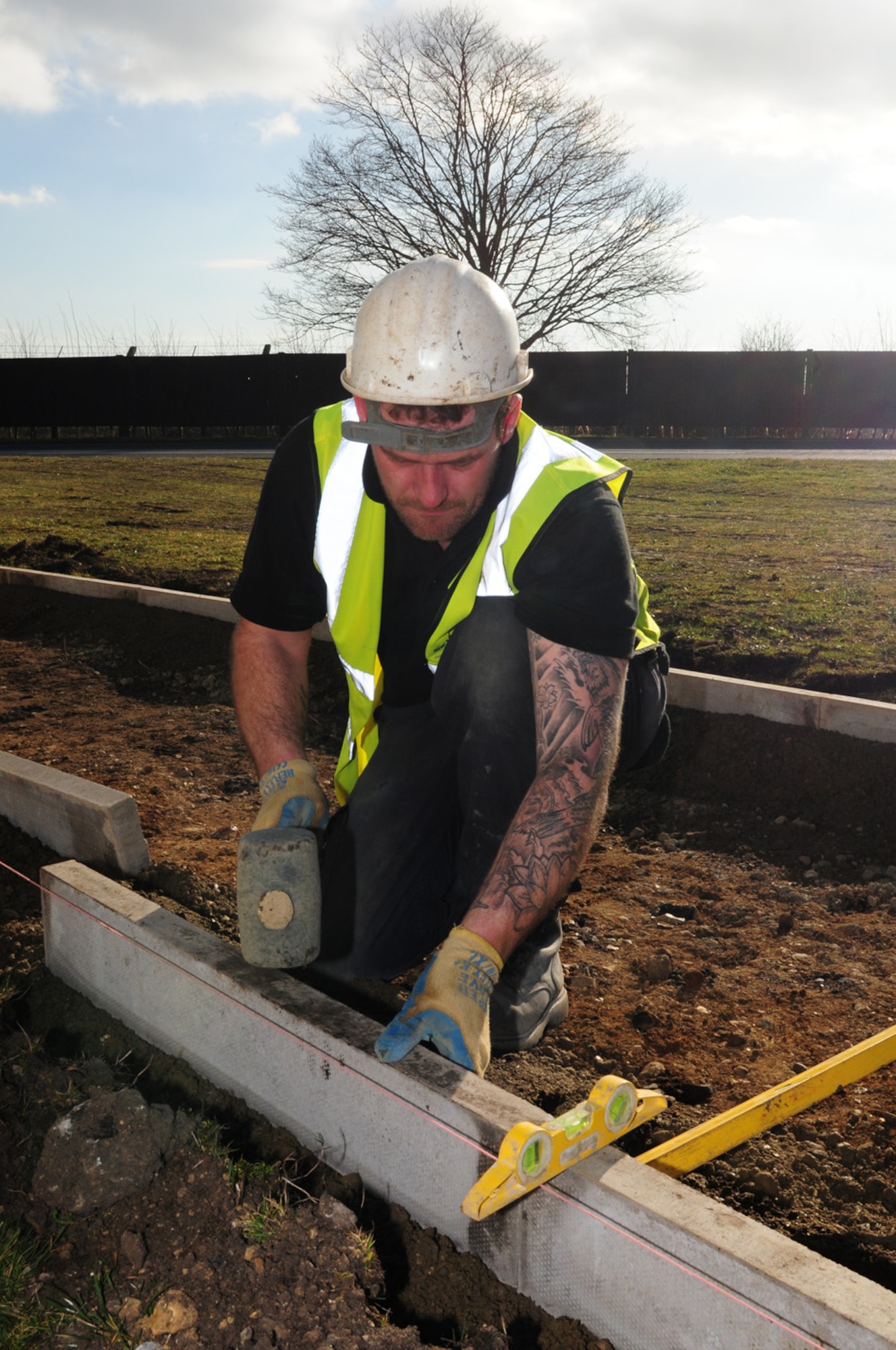 RAF MILDENHALL, England -- Gary Congreve, a contractor, lays path edgings on the new running track Feb. 23, 2012. The path will run mainly along the perimeter road, from the south side sports field to Lincoln road, near the long-term parking lot. The total cost for the project is more than $634,000. It will be about 6-feet-wide and is scheduled for completion in June. The construction project is using recycled, crushed concrete from the demolition of Building 538 and recycled rubber (from vehicle tires) for the top surface. (U.S. Air Force photo/Karen Abeyasekere)
