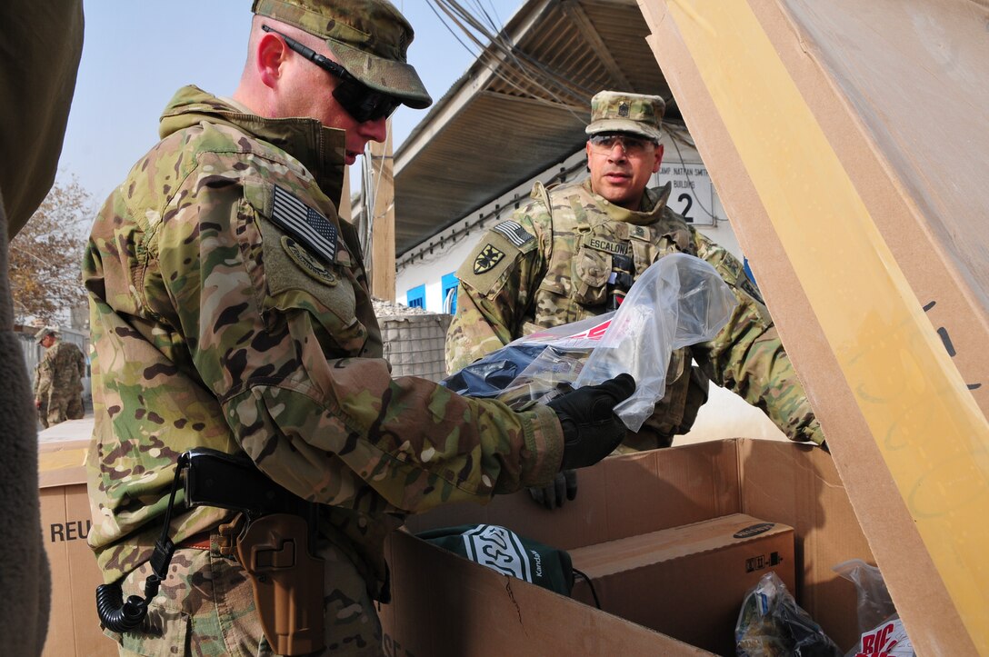 Command Sgt. Maj. Tony Escalona (right), command sergeant major, Task Force Resolute shows Sgt. Maj. Kevin Muhlenbeck, operations sergeant major, Task Force Bison some of the gifts donated by the USO for his Soldiers during Operation Christmas Convoy at Camp Nathan Smith Dec. 23. Operation Christmas Convoy delivered gifts to Soldiers on remote forward operating bases for the holiday season. (U.S. Army photo by Staff Sgt. Alexander Burnett)