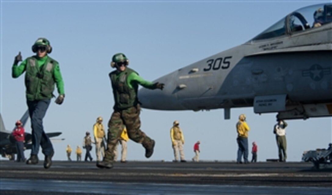 Petty Officers 3rd Class Chord Deckert and Adam Fitzgerald clear the launching area as an F/A-18C Hornet from Strike Fighter Squadron 97 prepares to launch off the flight deck of the aircraft carrier USS John C. Stennis (CVN 74) in the Arabian Sea on Jan. 1, 2012.  The John C. Stennis is deployed to the U.S. 5th Fleet area of responsibility conducting maritime security operations and support missions as part of Operation Enduring Freedom.  