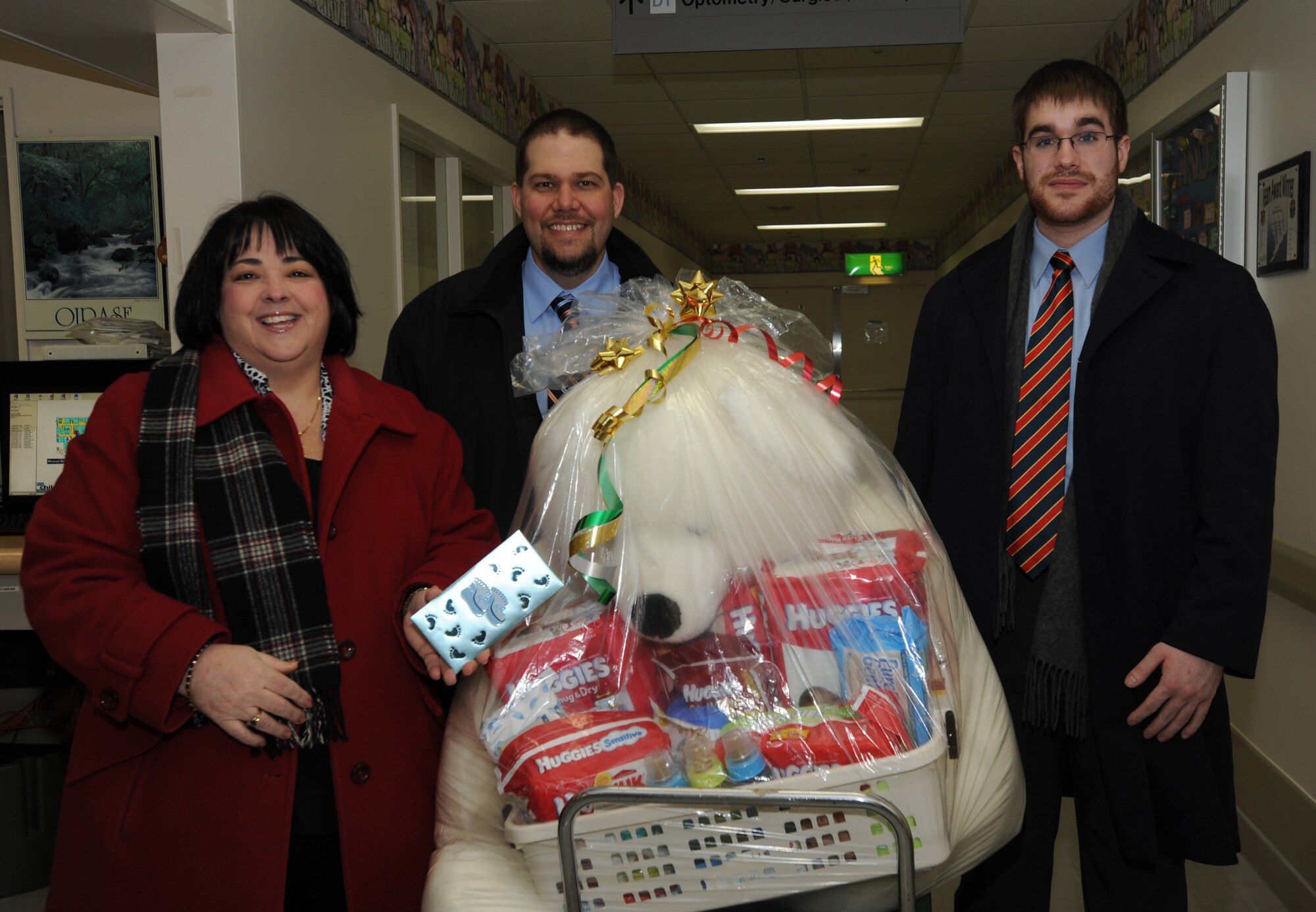 MISAWA AIR BASE, Japan – In recognition of the first 2012 baby to be delivered at Misawa, members of the Misawa Air Base community present gifts to the Hawkins family at the base hospital Jan. 3, 2012. To help the small family, Trish Reams, district manager for Web Co., Matthew Whittaker, office manager for base commissary (middle), and Caleb Houdek, independent sales representative for Exchange New Car Sales brought a large teddy bear, diapers and other gifts for little Adam. (U.S. Air Force photo/Airman Kenna Jackson)