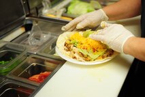 Jean Ballard, Three Eagles Golf Course snack bar head cook, adds requested toppings to a grilled chicken wrap on Seymour Johnson Air Force Base, N.C., Jan. 3, 2012. Ballard has worked at the snack bar for over ten years and enjoys working with her co-workers. Ballard is a native of Seven Springs, N.C. (U.S. Air Force photo by Senior Airman Rae Perry)