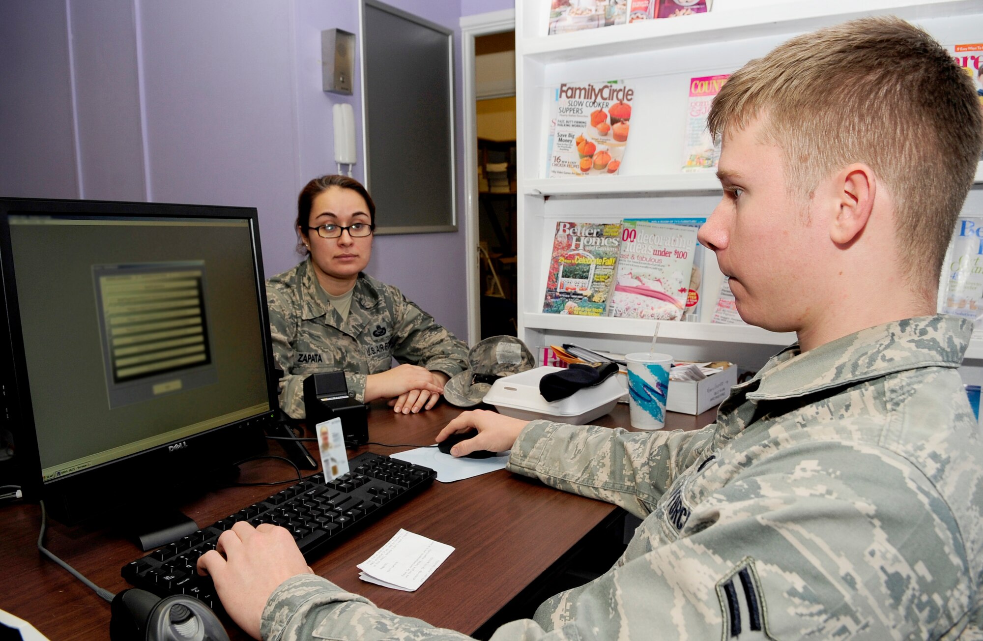 RAF MILDEHALL, England – Airman 1st Class Cody Gant (right), 100th Security Forces Squadron installation access control clerk, assists Master Sgt. Rosalba Zapata, 100th Force Support Squadron, with entering her military ID into the new installation access control system at the Bob Hope Community Center here Jan. 4, 2012. The new “IACS” system is being implemented across U.S. Air Forces in Europe to meet security requirements. (U.S. Air Force photo/Senior Airman Ethan Morgan) (Photo masked for security purposes)