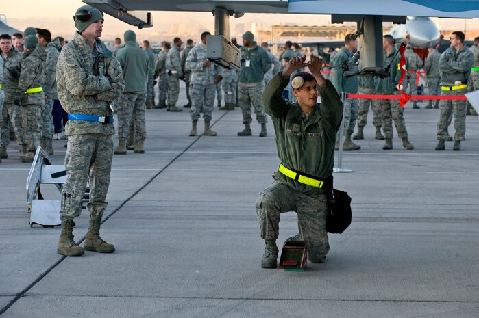 U.S. Air Force Airman Robert Lapp 57th Aircraft Maintenance Squadron aircraft armament systems journeyman, prepares an F-16 Fighting Falcon for bomb loading while Staff Sgt. Justin Vandevander, 57th Maintenance Squadron, judges Airman Lapp during the quarterly weapons load competition Jan. 6, 2012, at Nellis Air Force Base, Nev. Weapons load competitions are conducted quarterly to keep Airmen sharp and recognize superior performers. Weapons load teams are evaluated for use of the checklist, safety, and overall speed. (U.S. Air Force photo by Staff Sgt. William P.Coleman/Released)  