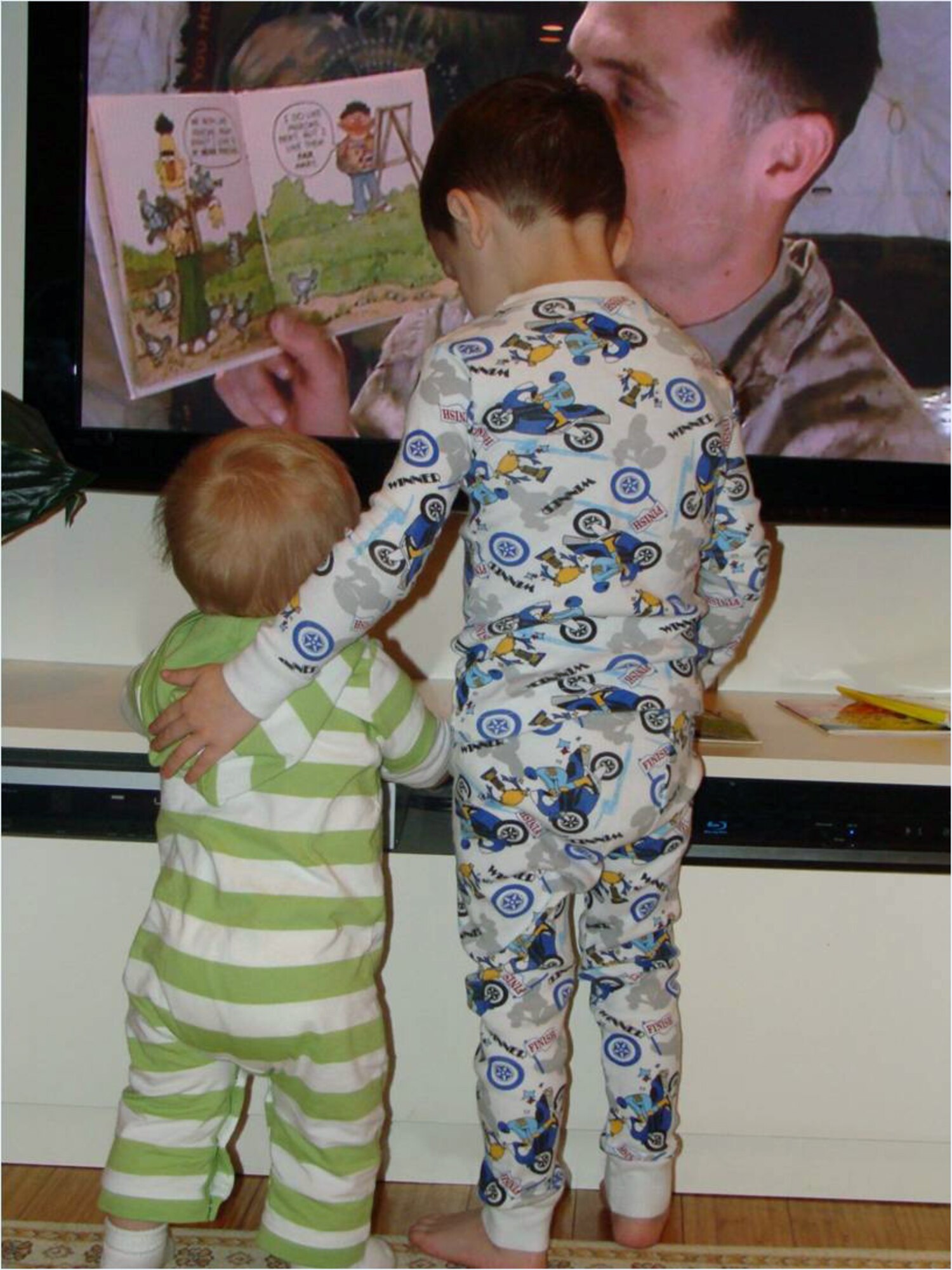 Two children in the United States watch a video recorded by their deployed father who used the United Services Organization’s United Through Reading service at Bagram Airfield, Aghanistan.  The USO records deployed servicemembers reading to their loved ones and sends the DVD and book back to the member's home.  (U.S. Air Force courtesy photo)