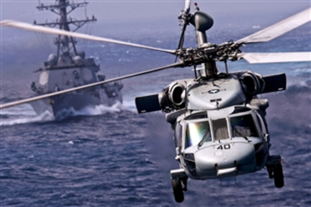 An MH-60S Knight Hawk helicopter passes the USS Chafee (DDG 90) while delivering supplies to the USS Carl Vinson (CVN 70) during a vertical replenishment mission with the USNS Bridge in the Pacific Ocean on Jan. 2, 2012.  