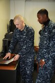 Petty Officer 3rd Class Ryan Davis watches as Petty Officer 2nd Class Eric Martin places the Standard Form 87 fingerprint card into an Identaprint machine which heats the paper and red ink, allowing the finished result to appear black in color. Martin is a Machinist’s Mate assigned to the 628th Security Forces Squadron Information Protection Office at Joint Base Charleston – Weapons Station and Davis is a Ship’s Serviceman assigned to Naval Support Activity’s Unaccompanied Personnel Housing office at JB Charleston-Weapons Station. (U.S. Navy photo/Petty Officer 1st Class Jennifer Hudson)