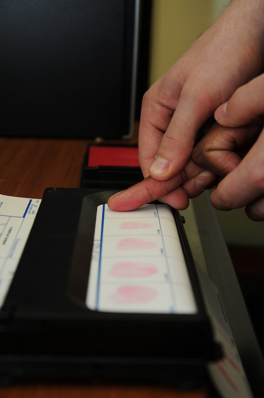 Petty Officer 2nd Class Eric Martin rolls Petty Officer 3rd Class Ryan Davis’s finger onto the fingerprint card at Naval Support Activity, Joint Base Charleston – Weapons Station. NSA began using the new inkless fingerprinting system in 2011. The inkless system provides a more detailed fingerprint and costs significantly less than the traditional black ink method which often failed as fingerprints sometimes smeared and became unusable. (U.S. Navy photo/Mass Communication Specialist 1st Class Jennifer Hudson)