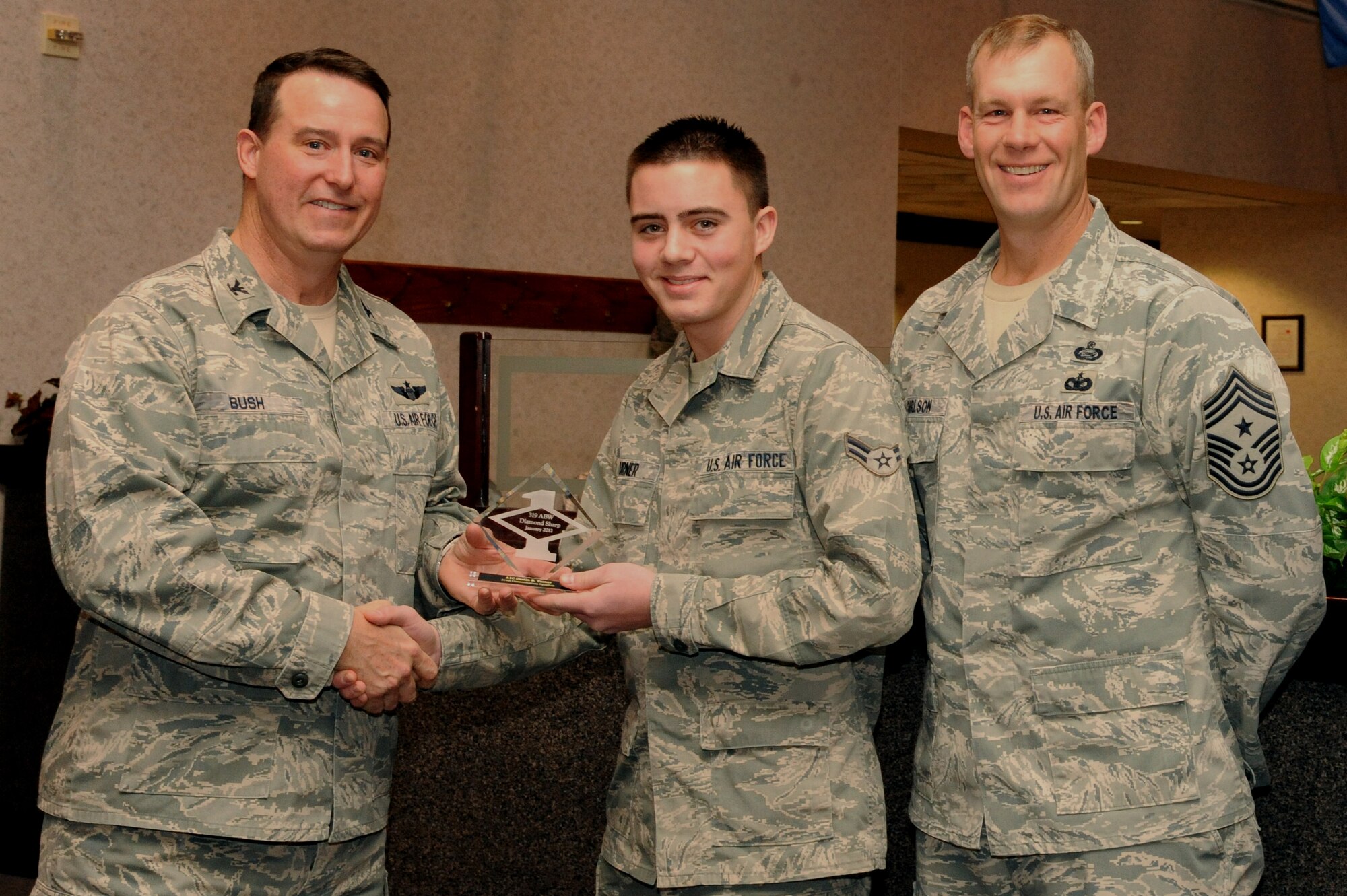Col. Timothy Bush, 319th Air Base Wing commander, presents Airman 1st Class Dustin Turner, 319th Communications Squadron, with a Diamond Sharp Award Jan. 10 on Grand Forks Air Force Base, N.D., accompanied by 319th ABW Command Chief Master Sgt. David Carlson. The Diamond Sharp Award is given to Airmen who epitomize service before self and strive for excellence at work and off duty. (U.S. Air Force photo by Airman 1st Class Xavier Navarro)