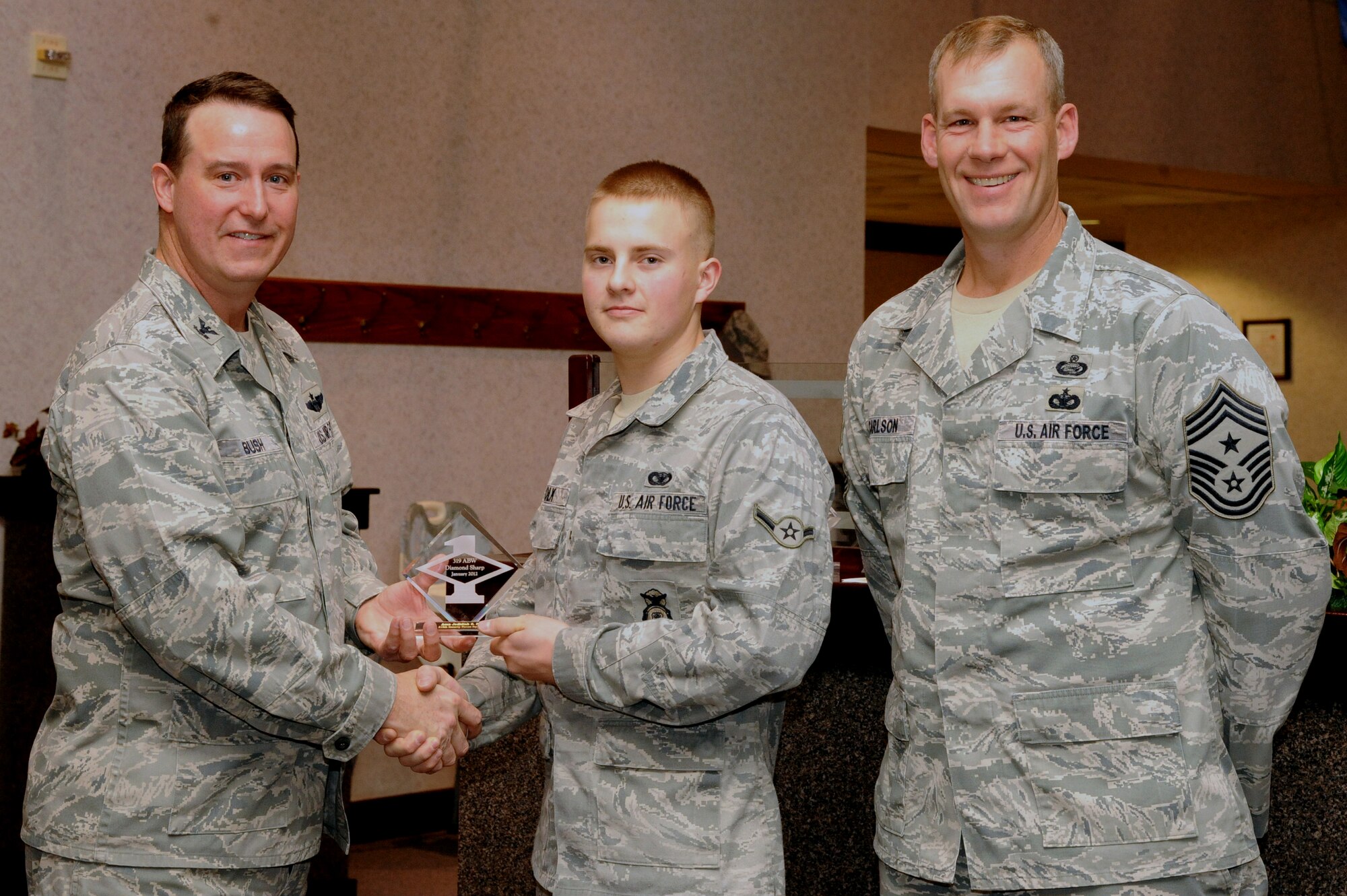 Col. Timothy Bush, 319th Air Base Wing commander, presents Airman Jedidiah Polk, 319th Security Forces Squadron, with a Diamond Sharp Award Jan. 10 on Grand Forks Air Force Base, N.D., accompanied by 319th ABW Command Chief Master Sgt. David Carlson.  The Diamond Sharp Award is given to Airmen who epitomize service before self and strive for excellence at work and off duty.  (U.S. Air Force photo by Airman 1st Class Xavier Navarro)
