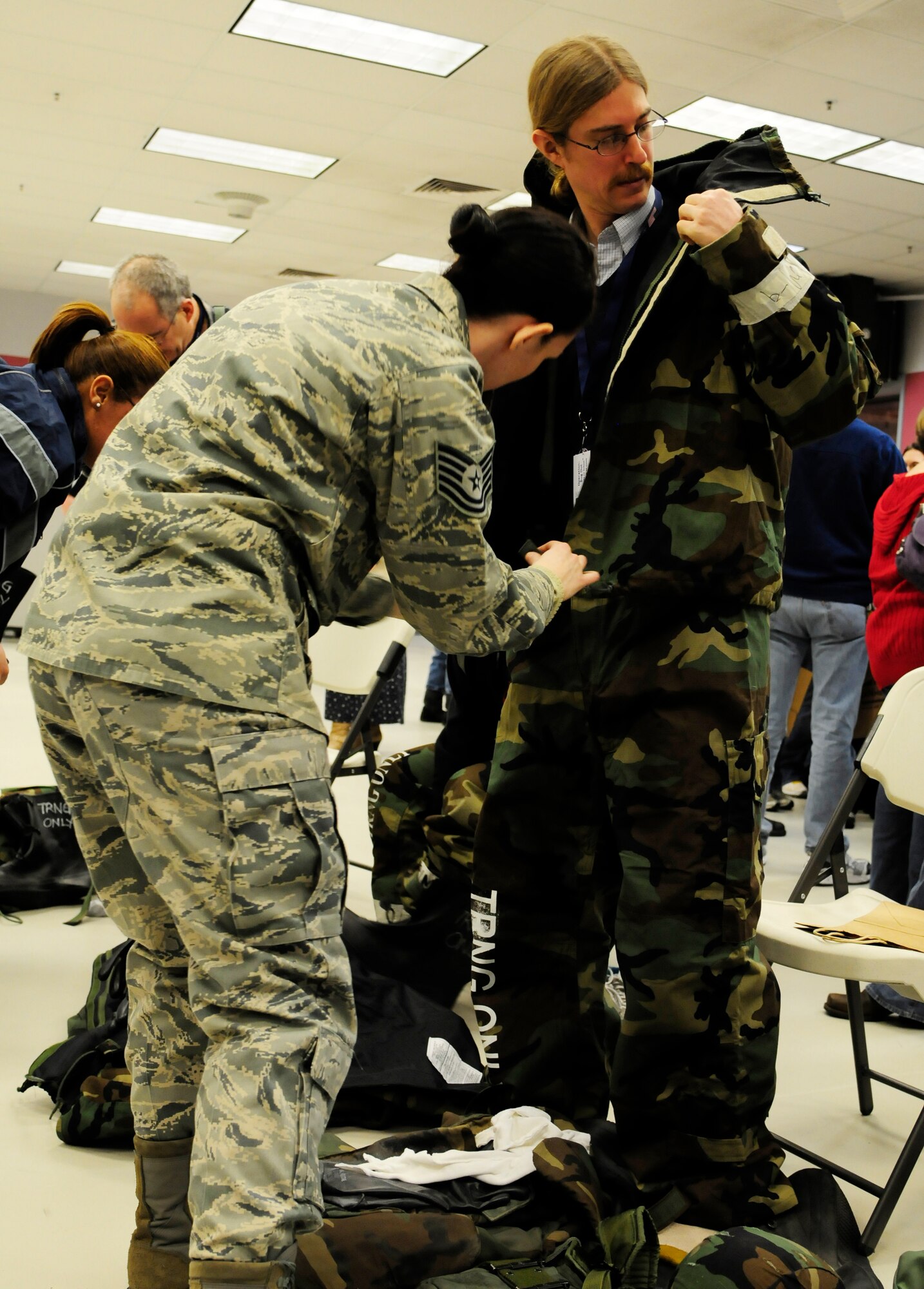U.S. Air Force Tech. Sgt. Kristy Raso, 354th Medical Operation Squadron NCO in charge of flight medicine, helps an educator properly wear chemical gear Jan. 6, 2012, Eielson Air Force Base, Alaska. Operation Bug Out gave educators from North Pole and Eielson an opportunity to try on chemical gear used in a deployed location to protect servicemembers against harmful chemical agents. (U.S. Air Force photo by Airman 1st Class Yash Rojas/Released)