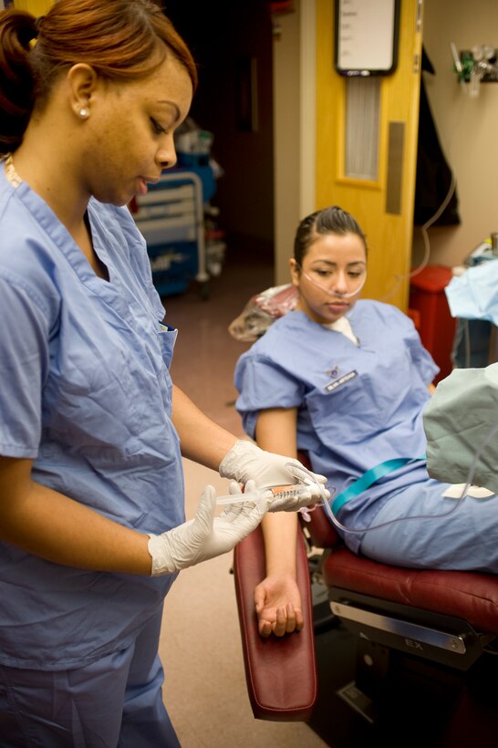 Staff Sgt. Natosha Mansker, 779th Dental Squadron Maxillofacial Surgery Clinic NCO in charge of Oral Surgery, simulates pushing sedation medication through an intravenous line toward Senior Airman Iris Silva-Arteaga, 779 DS dental technician, during surgical training at the Andrews dental clinic Jan. 10. (Photo /Bobby Jones)