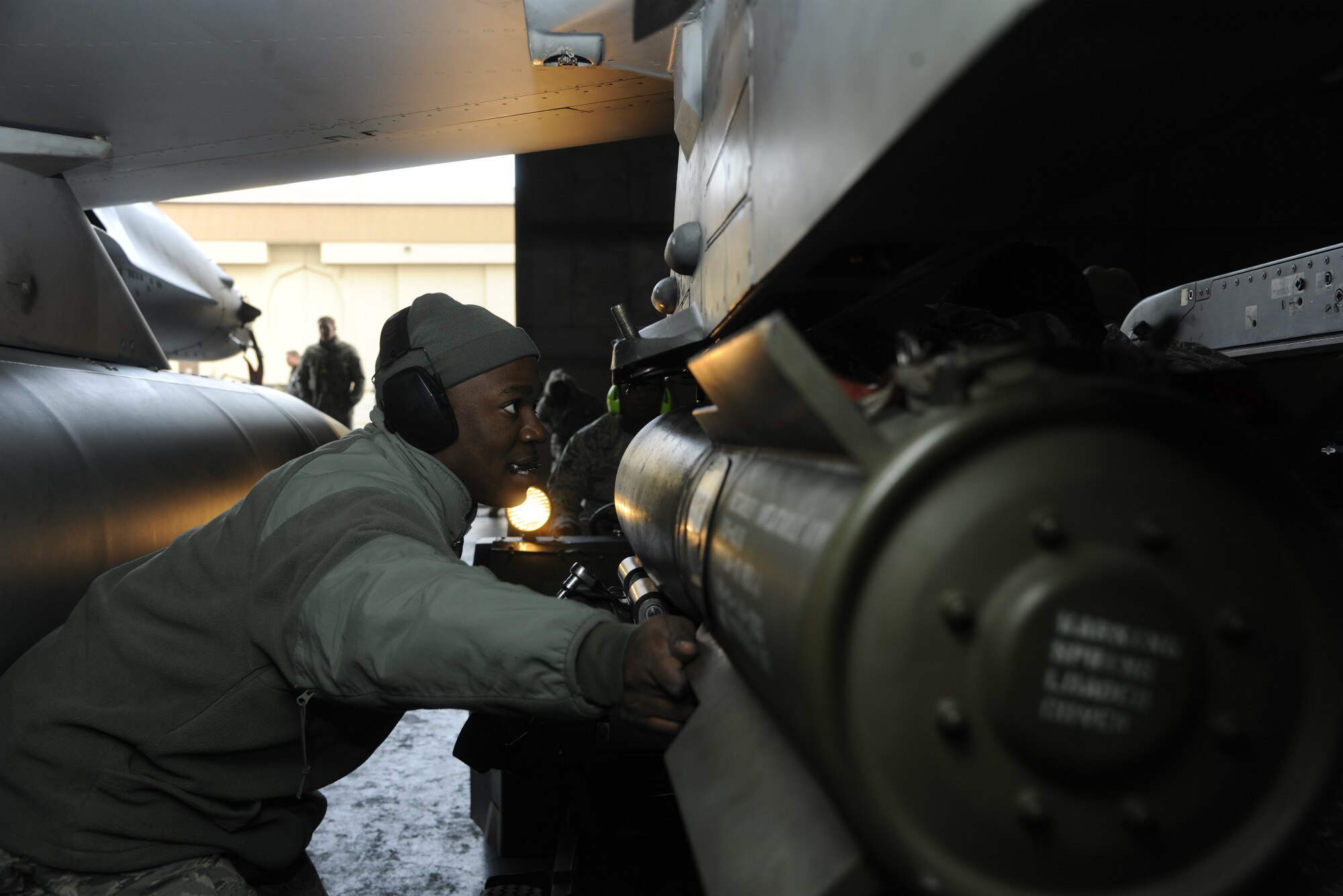 Staff Sgt. Kenneth Williams, 35th Aircraft Maintenance Unit weapons load crew member, assists in lining up a weapon as it is loaded under the wing of an F-16 Fighting Falcon during a peninsula weapons loading competition at Kunsan Air Base, Republic of Korea, Jan. 11, 2012. Each team raced against time loading training weapons on their respective F-16 Fighting Falcons trying to minimize discrepancies. The training of the teams improves job performance, but it also fosters teamwork and camaraderie. (U.S. Air Force photo by Staff Sgt. Rasheen A. Douglas/Released)