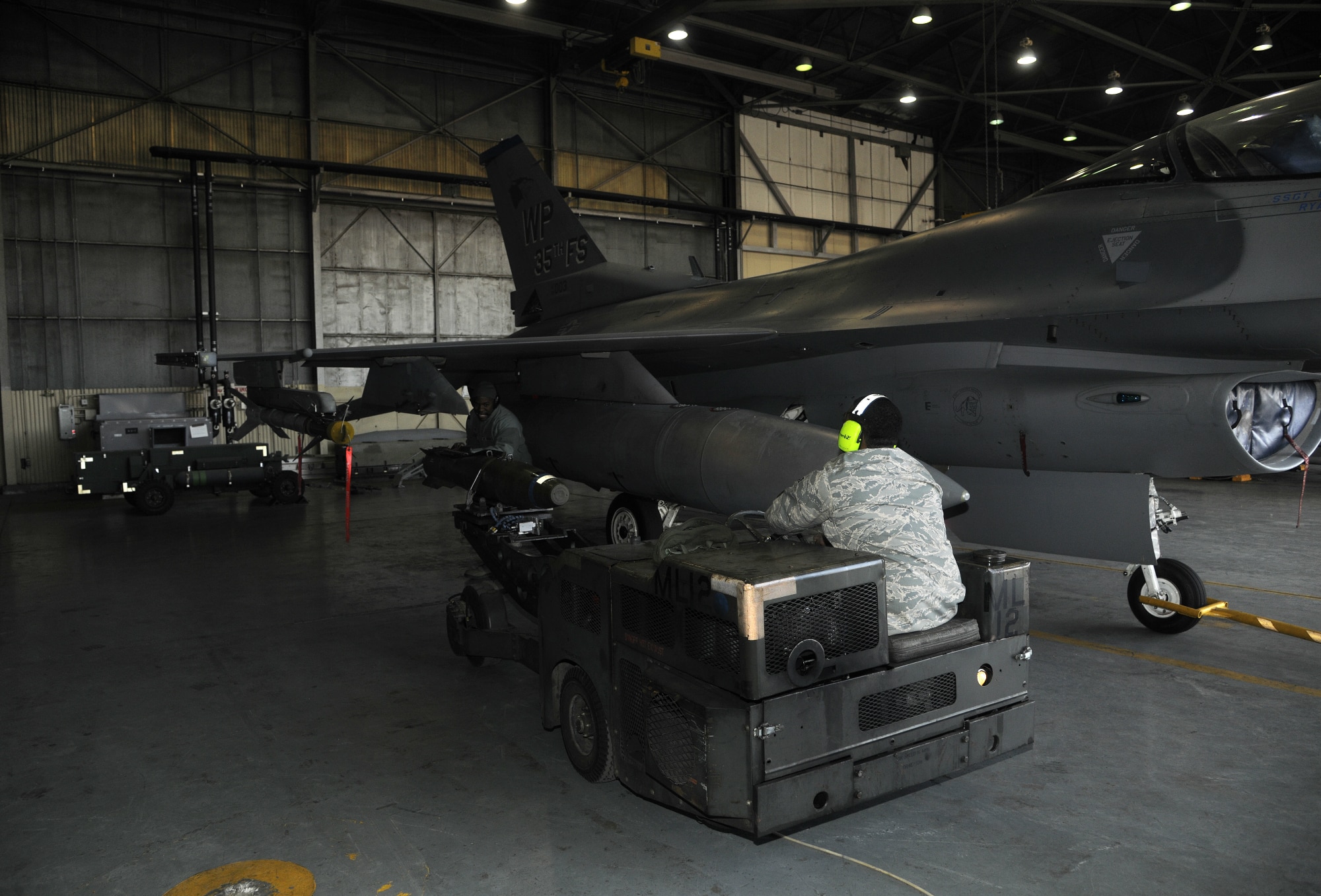 Staff Sgt. Kenneth Williams, guides Senior Airman Demarcus Kirby, 35th Aircraft Maintenance Unit weapons load crew members, driving an MJ1 bomb lift truck to load a weapon onto an F-16 Fighting Falcon during a peninsula weapons loading competition at Kunsan Air Base, Republic of Korea, Jan. 11, 2012. Each team raced against time loading training weapons on their respective F-16 Fighting Falcons trying to minimize discrepancies. The training of the teams improves job performance, but it also fosters teamwork and camaraderie. (U.S. Air Force photo by Staff Sgt. Rasheen A. Douglas/Released)