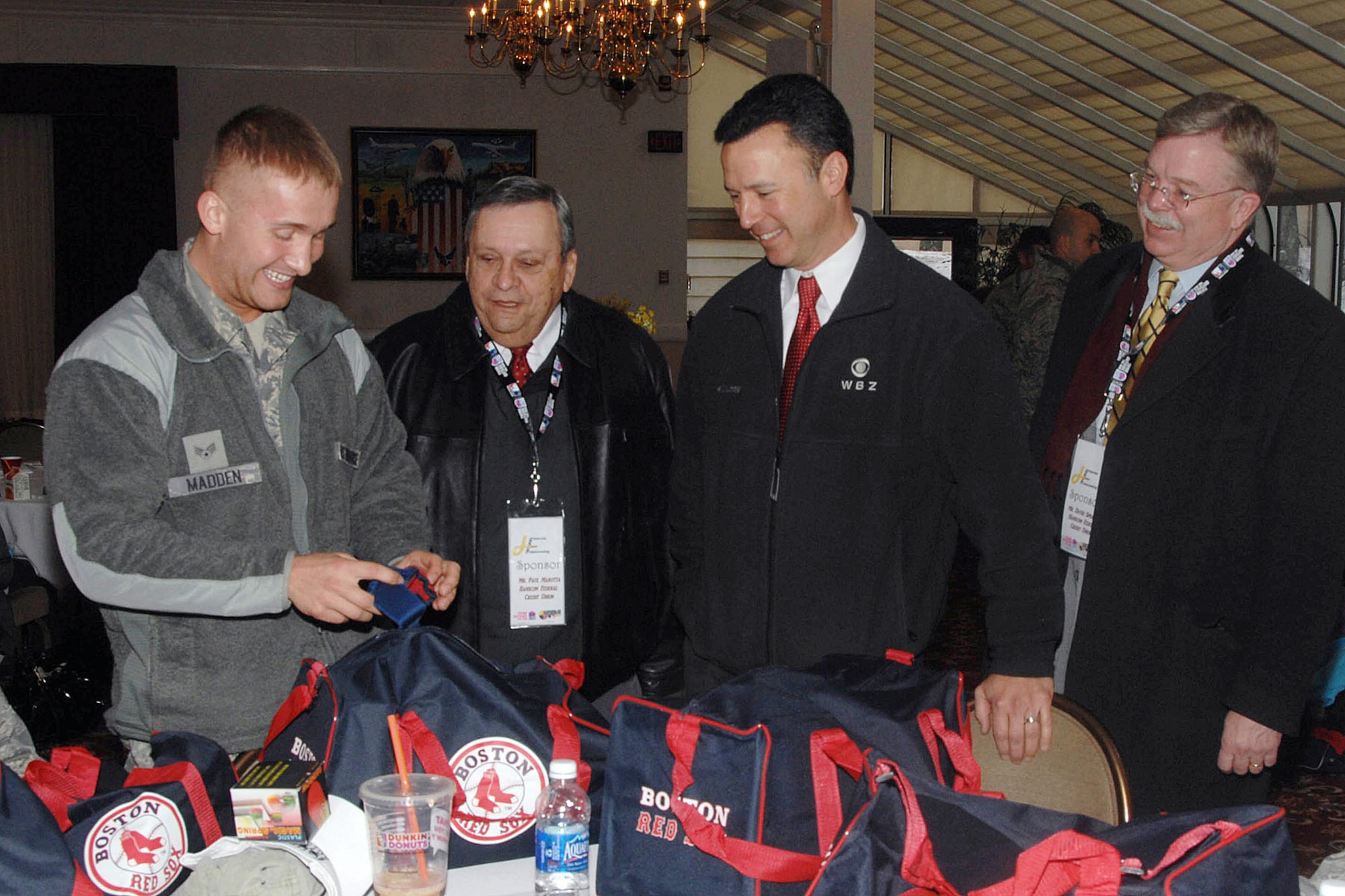 HANSCOM AIR FORCE BASE, Mass. -- Senior Airman Kyle Madden (left), from the 66th Security Forces Squadron, is all smiles as he shows Paul Marotta, Hanscom Federal Credit Union chairman; Jonathan Elias, WBZ-TV anchor; and David Spraque, Hanscom Federal Credit Union CEO, items he recieved from donations made to Airmen returning from deployments. Madden was one of 54 Airmen who have returned home from a deployment in the past six months honored during the Heroes Homecoming celebration Jan. 12. (U.S. Air Force photo by Linda LaBonte Britt) 