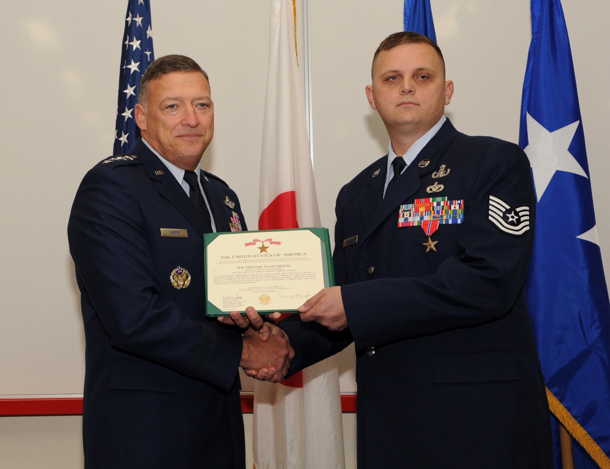 U.S. Air Force Gen. Gary North, Pacific Air Forces commander, presents U.S. Air Force Tech. Sgt. John Johnson, 18th Civil Engineer Squadron Explosive Ordnance Disposal (EOD) craftsman, with a Bronze Star Medal citation at Kadena Air Base, Japan, Jan. 9, 2012. Johnson was awarded the Bronze Star Medal for exceptionally meritorious service as an EOD Team Leader while deployed in support of Operation Enduring Freedom. (U.S. Air Force photo by Senior Airman Jarvie Z. Wallace/Released) 
