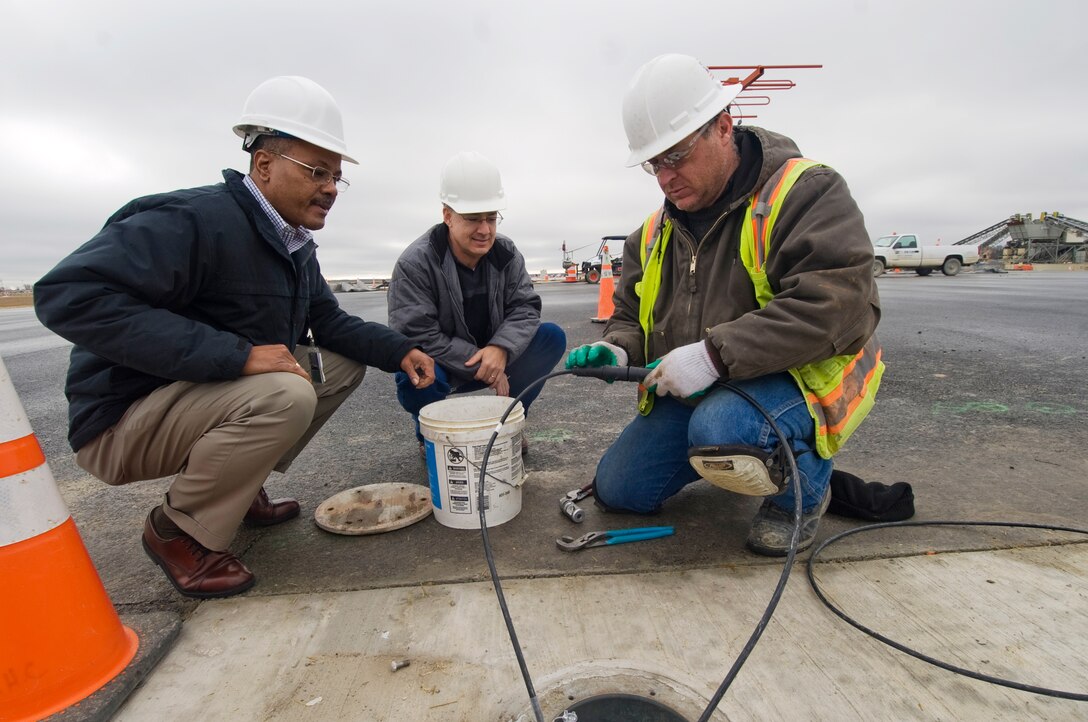 Mike Butts and Max McAllister, 11th Civil Engineer Squadron electrical engineer technicians, help Ion Ene, a contract electrician, spot check equipment, as he prepares to splice wire to repair an inoperative airfield runway light Jan. 12.  (Photo /Bobby Jones)