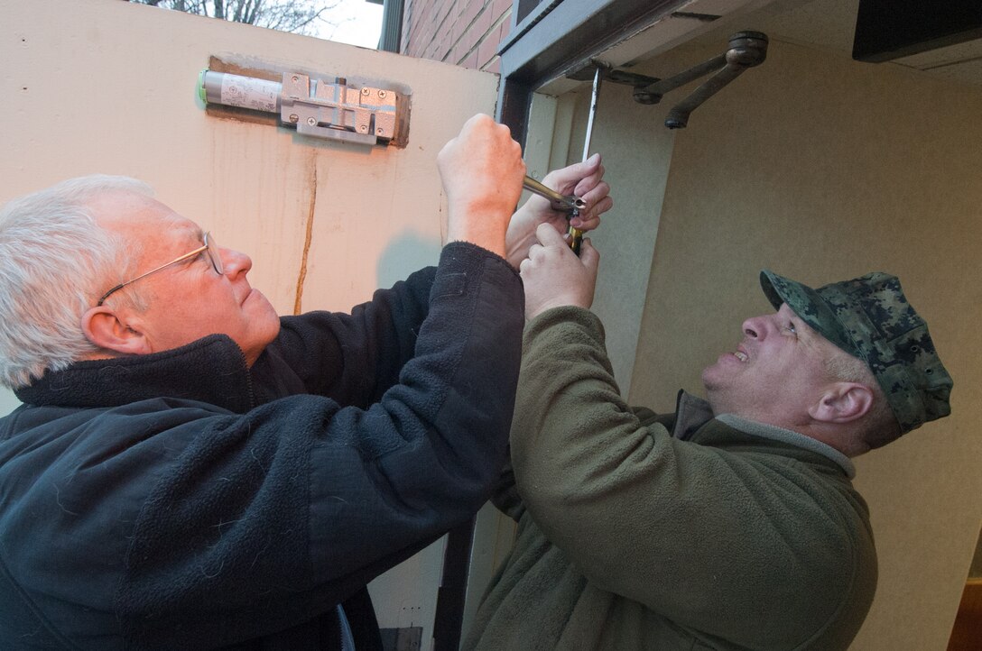 Gary Spencer, 11th Civil Engineer Squadron carpenter, and Tim McGraw, maintenance mechanic, apply pressure to loosen a  frozen screw to replace a hydraulic door closer at the 11 CES headquarters building Jan. 12. (Photo/Bobby Jones)