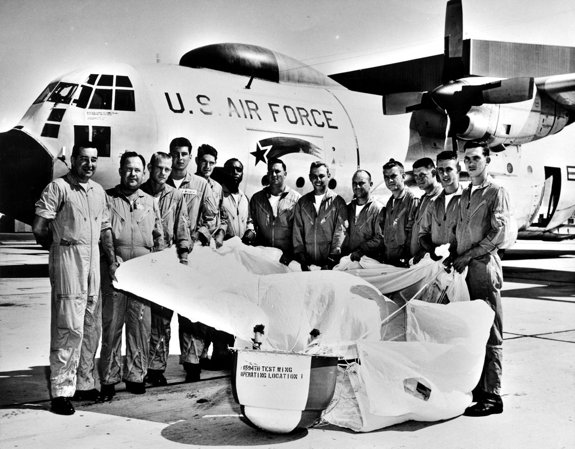 Airmen of the 6594th Test Wing with a practice satellite payload. Note the falling star logo on their JC-130B Hercules aircraft. (U.S. Air Force photo)