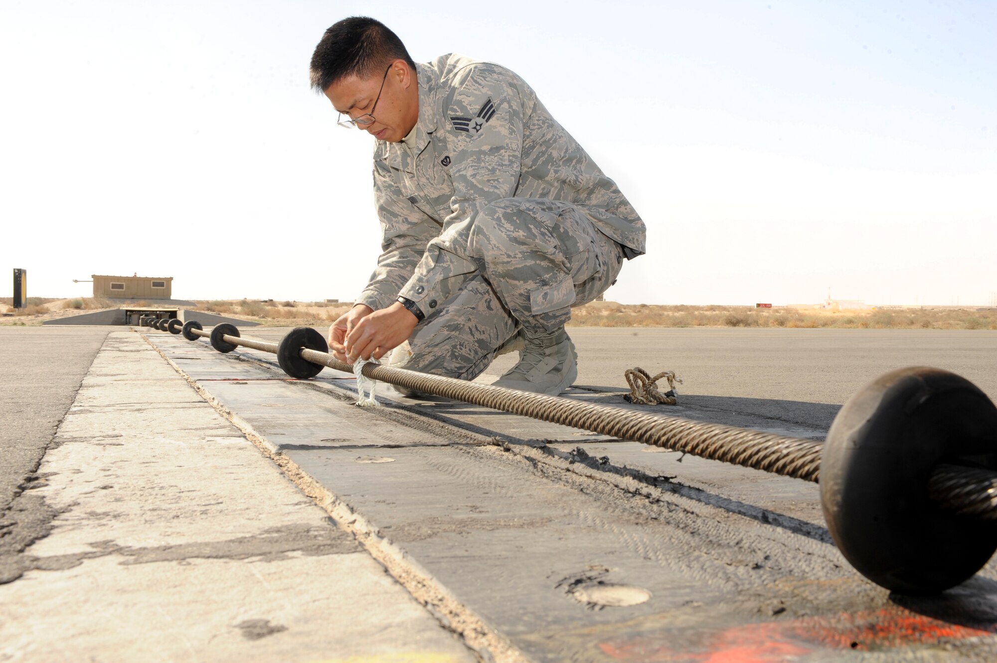 Senior Airman Ephesians Bagorio, 332nd Expeditionary Civil Engineer Squadron, applies a new rope to the barrier arresting kit on a runway at an undisclosed location in Southwest Asia, Jan. 12, 2012. Bagorio is one of two personnel who graduated from the Hawaii National Guard Youth Challenge Academy on base. The YCA taught Bagorio core competencies that he uses in his daily. Bagorio is native to Hawaii and is deployed from Davis-Monthan Air Force Base, Ariz. (U.S. Air Force photo by Staff Sgt. Joshua J. Garcia/Released)