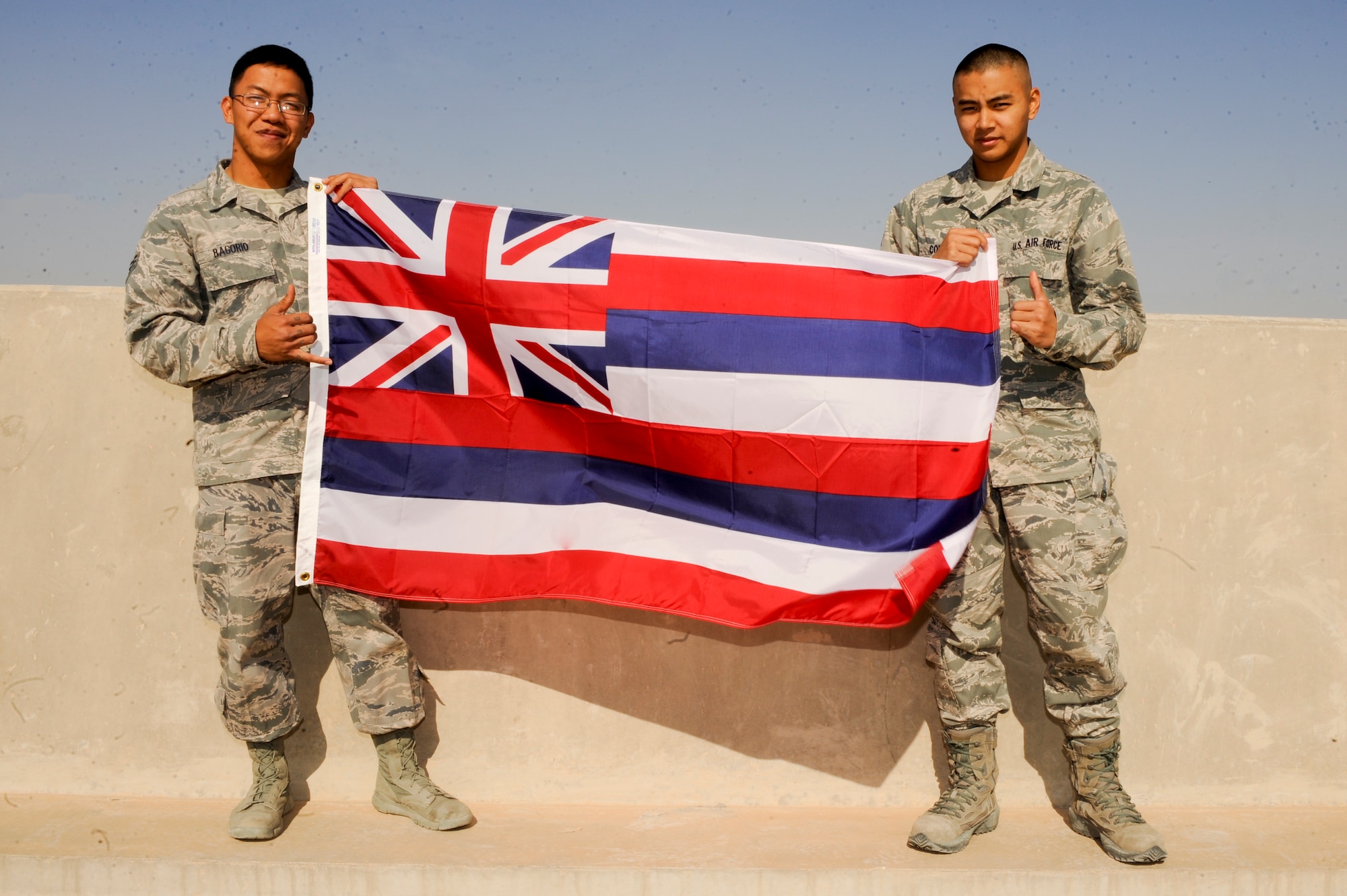 Senior Airman Ephesians Bagorio, 332nd Expeditionary Civil Engineer Squadron, and Airman 1st Class Kameron Combis, 332nd Expeditionary Communications Squadron, hold the Hawaiian state flag at an undisclosed location in Southwest Asia, Jan. 20, 2012. Bagorio and Combis graduated together from Barber's Point Campus of the Hawaii National Guard Youth Challenge Academy. The academy is a 'quasi-military' program that helps misguided youth to become a working part of the community. Bagorio is deployed from Davis-Monthan, Ariz., and Combis is deployed from the Hawaii Air National Guard. Both are native to the state of Hawaii. (U.S. Air Force photo by Staff Sgt. Joshua J. Garcia/Released)