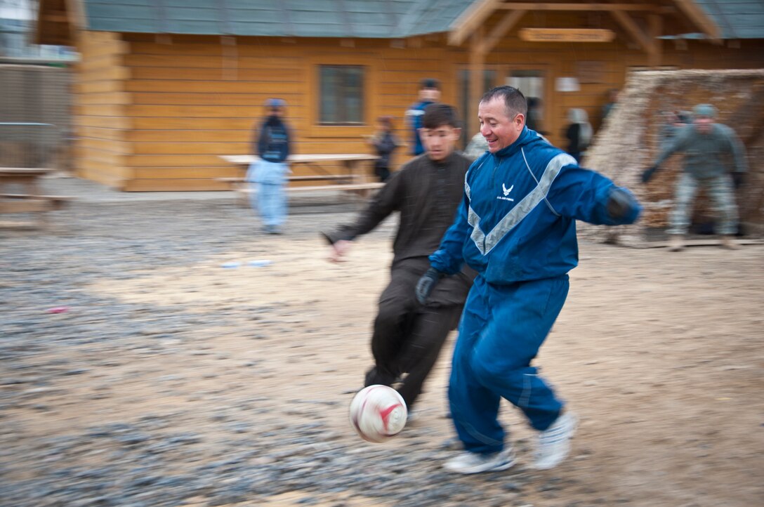 KANDAHAR AIRFIELD, Afghanistan -- Staff Sgt. David Medina, 451st Expeditionary Civil Engineer Squadron, runs after a loose ball during the weekly soccer game against the bazaar school children at Kandahar Airfield, Afghanistan Jan. 21, 2012. Volunteers from various 451st Air Expeditionary Wing units play against the children every week to promote physical fitness and camaraderie.  (U.S. Air Force photo by Staff Sgt. David Carbajal)