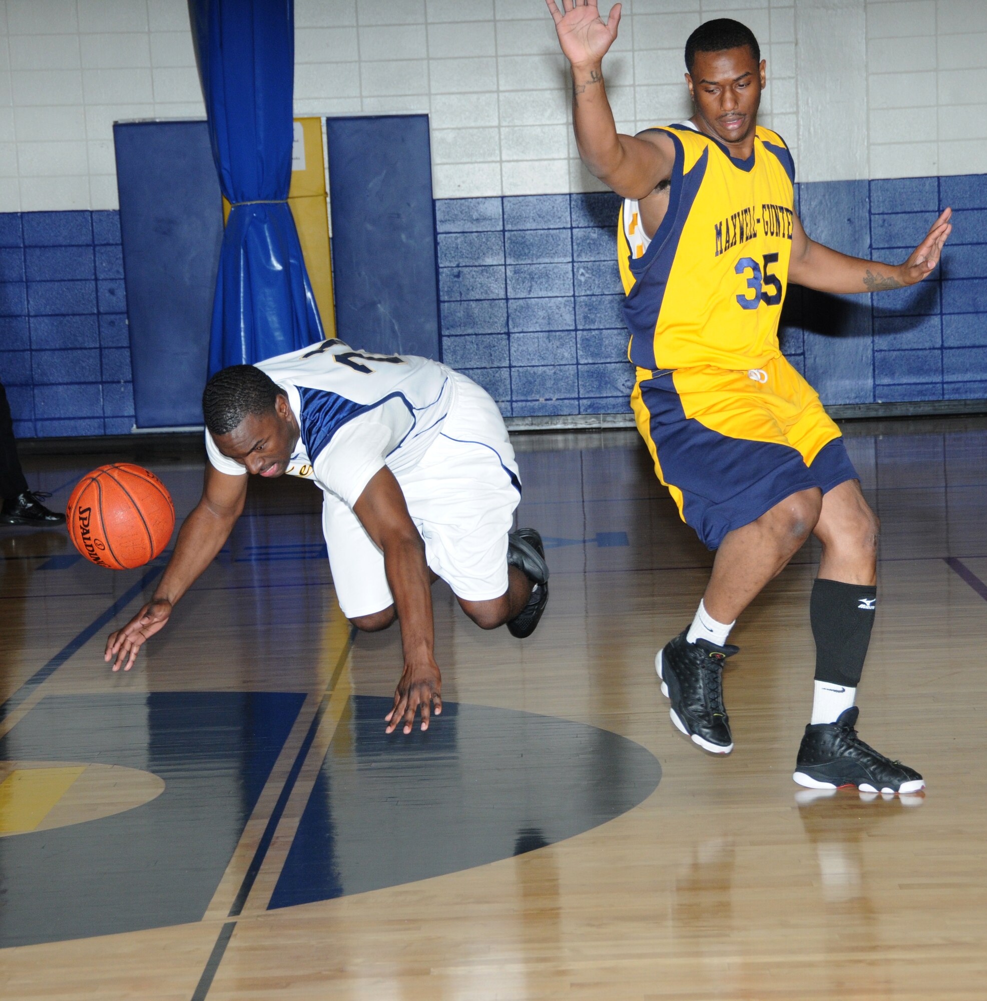Keesler Dragon Tony Whitley dives to recover a loose basketball as Andrew Williams, Maxwell-Gunter Air Force Base, Ala., turns in the same direction during a Southeastern Military Athletic Conference varsity basketball game Jan. 21, 2012, at the Blake Fitness Center, Keesler Air Force Base, Miss.  The Maxwell-Gunter Warriors defeated the Keesler Dragons, 73-69. (U.S. Air Force photo by Kemberly Groue)