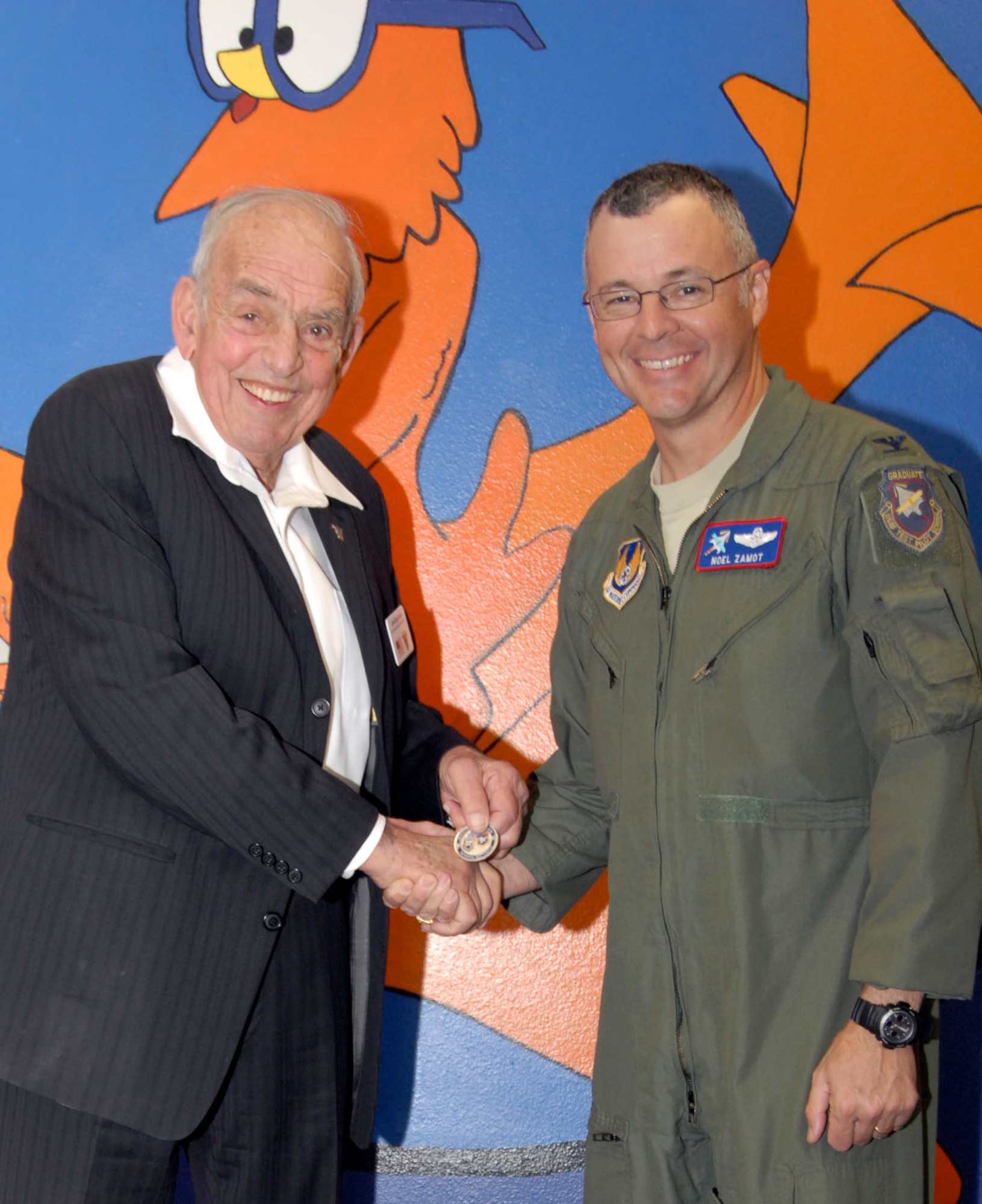 Col. Noel Zamot, commandant, USAF Test Pilot School, presented Maj. Gen. James I. Baginski, USAF (retired) with a commander's coin after the general presentation spoke to TPS students about the critical role of air mobility and it's unique history Jan. 20. Even after retirement and 30 years of service, General Baginski continues to work on improving the Air Force's global airlift capability. (U.S. Air Force Photo by Laura Mowry)