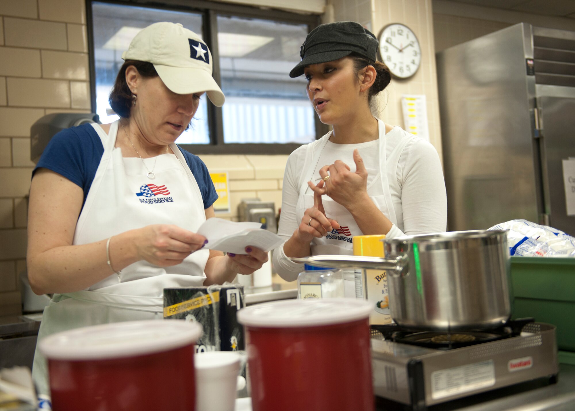Lisa Pearce and Kristen Tateishi of team “Sass with Class” quickly discuss ideas before competition start time begins during the winter wonderland themed Cupcake Wars at the Georgia Pines Dining Facility Jan. 24, 2012 at Moody Air Force Base, Ga. The event consisted of five teams that had ten minutes to gather supplies and one hour to cook, decorate and plate three different types of cupcakes. (U.S. Air Force photo by Senior Airman Eileen Meier/Released)