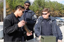 Petty Officer 2nd Class Bradley Nguyen, left, shows Timothy Reed, right, and David Lettbetter an ammunition belt to verify the bullets were dummy rounds prior to conducting a crew-serve weapons training at the Federal Law Enforcement Training Center at Joint Base Charleston - Weapons Station, Jan. 19. Nguyen is a Gunner’s Mate assigned to the 628th Security Forces Squadron and is a range safety officer. Reed and Lettbetter are harbor patrol unit police officers (U.S. Navy photo/Petty Officer 2nd Class Jennifer Hudson) 

