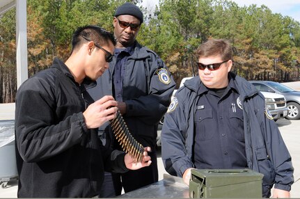 Petty Officer 2nd Class Bradley Nguyen, left, shows two harbor patrol unit police officers, Timothy Reed, right, and Lettbetter, center, an ammunition belt to verify the bullets were dummy rounds prior to conducting a crew-serve weapons training at the Federal Law Enforcement Training Center at Joint Base Charleston - Weapons Station, Jan. 19. Nguyen is a Gunner’s Mate assigned to the 628th Security Forces Squadron and is the range safety officer. (U.S. Navy photo/Petty Officer 2nd Class Jennifer Hudson)
