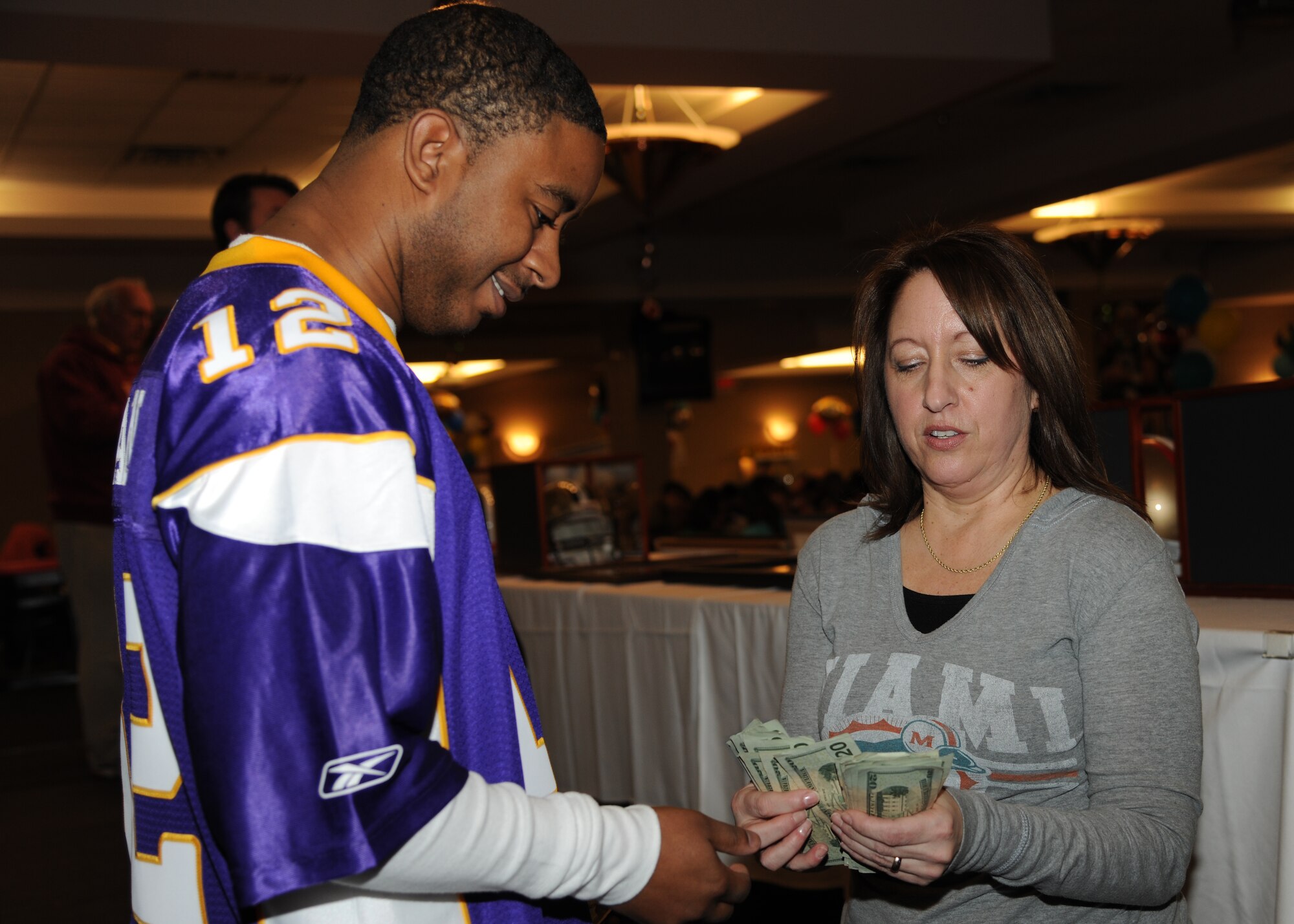 Paula Rheinhard, wife of Maj. Robert Reinhard, 319th Force Support Squadron commander, gives prize money to Staff Sgt. Brian Sheppard during the 6th annual Super Bowl Extravaganza Jan. 21, 2012, on Grand Forks Air Force Base, N.D.  Sheppard earned the money by auctioning off a Miami Dolphins jersey he won at the extravaganza. The 319th Force Support Squadron hosts the annual SBE to give the Grand Forks military and community members the opportunity to interact and win more than $38,000 in door prizes, including a chance to win a free trip to the Super Bowl or $5,000 cash. (U.S. Air Force photo/Airman 1st Class Ashley N. Taylor)