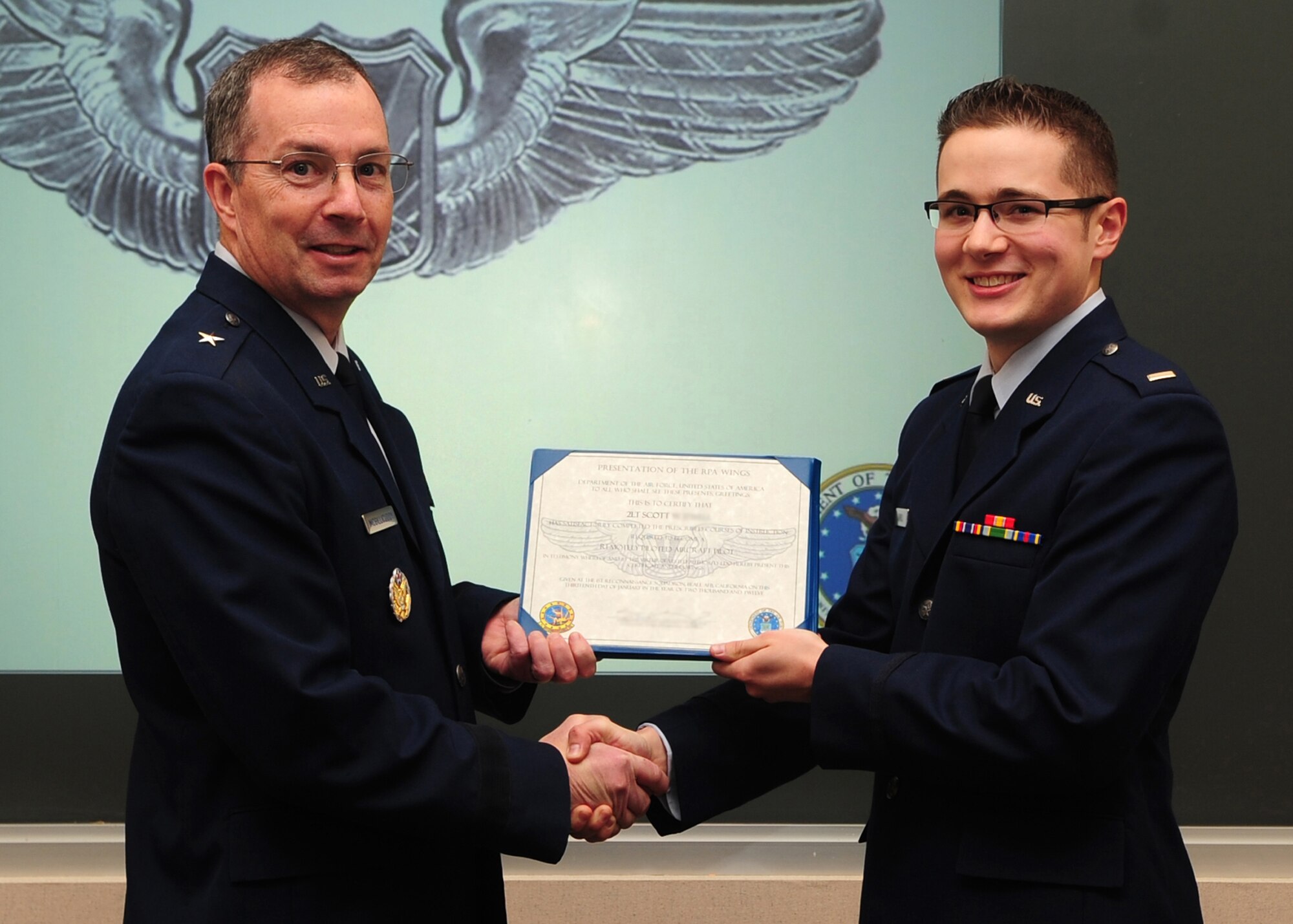 Brig. Gen. Paul McGillicuddy, 9th Reconnaissance Wing commander, presents a certificate to 2nd Lt. Scott during a winging ceremony at the 1st Reconnaissance Squadron's Dively Theater, Beale AFB, Calif., Jan. 13, 2012. 2nd Lt. Scott, along with 2nd Lt. Jacob, was one of the first two RQ-4 Global Hawk pilots to join the new 18X career field. (U.S. Air Force photo by Senior Airman Shawn Nickel/Released/Portions of this photo have been masked due to operational security reasons)